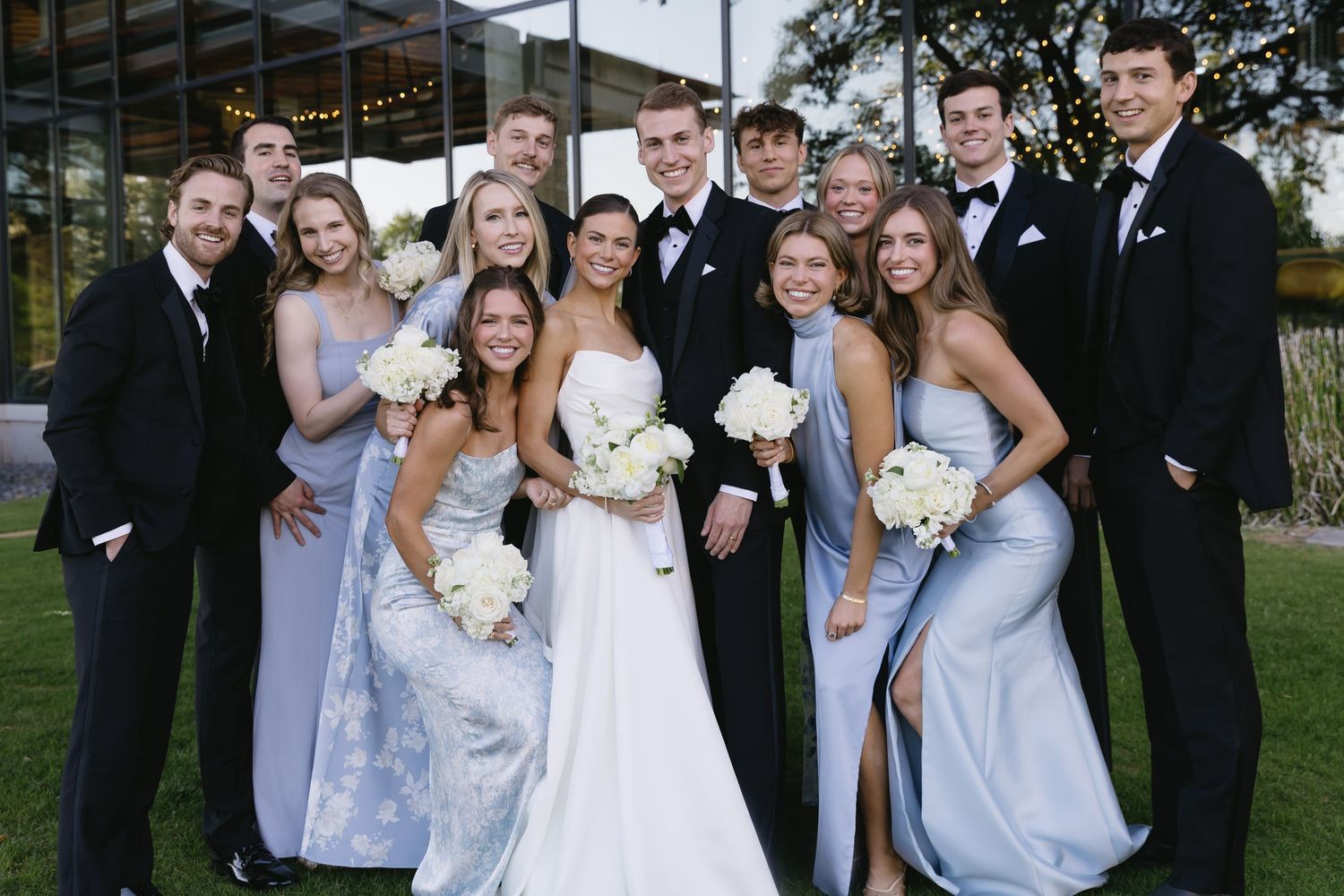 Wedding party photo with bridesmaids in light blue dresses and groomsmen in dark suits.