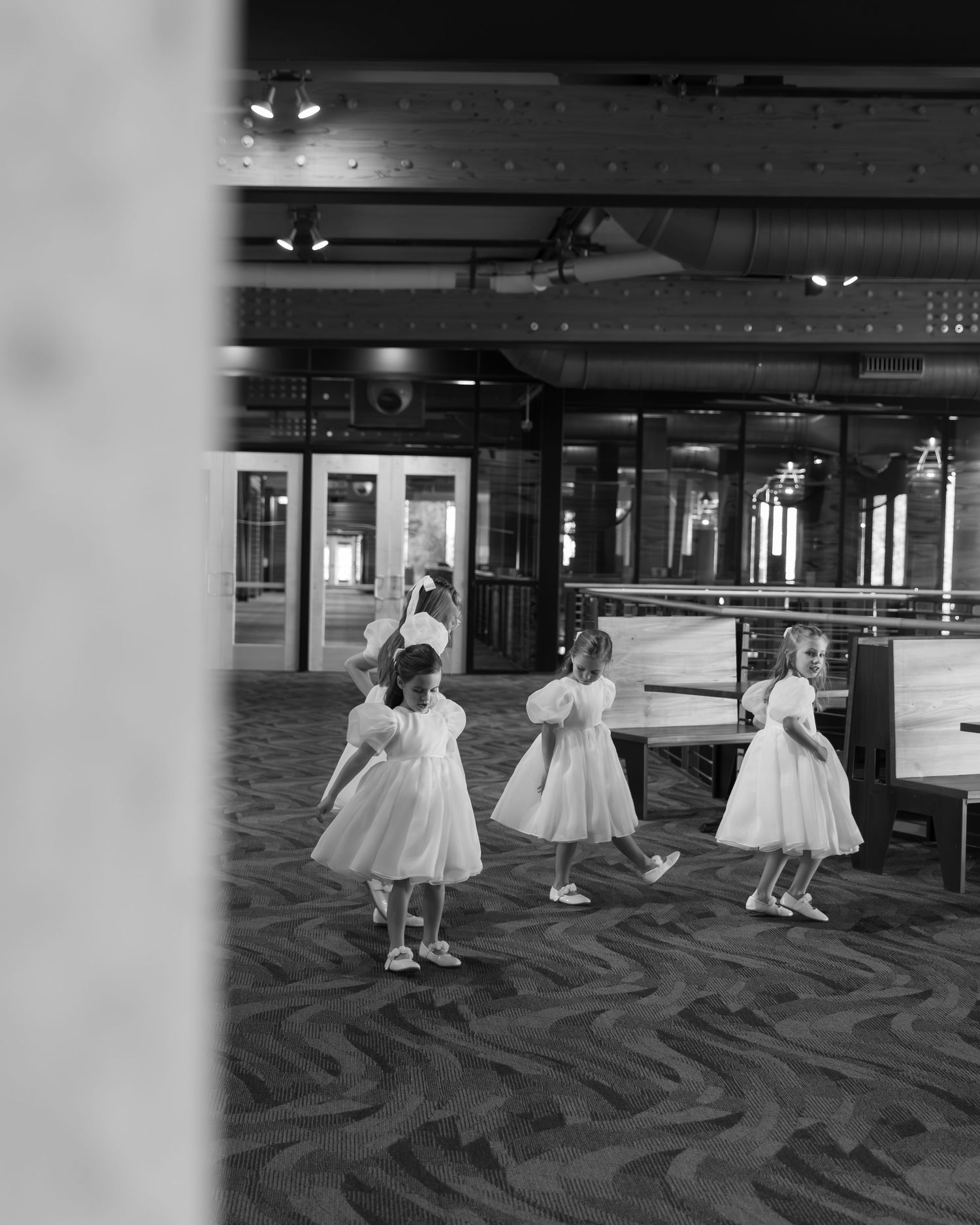 Young children in white dresses dancing and playing on a patterned carpet at a wedding reception.