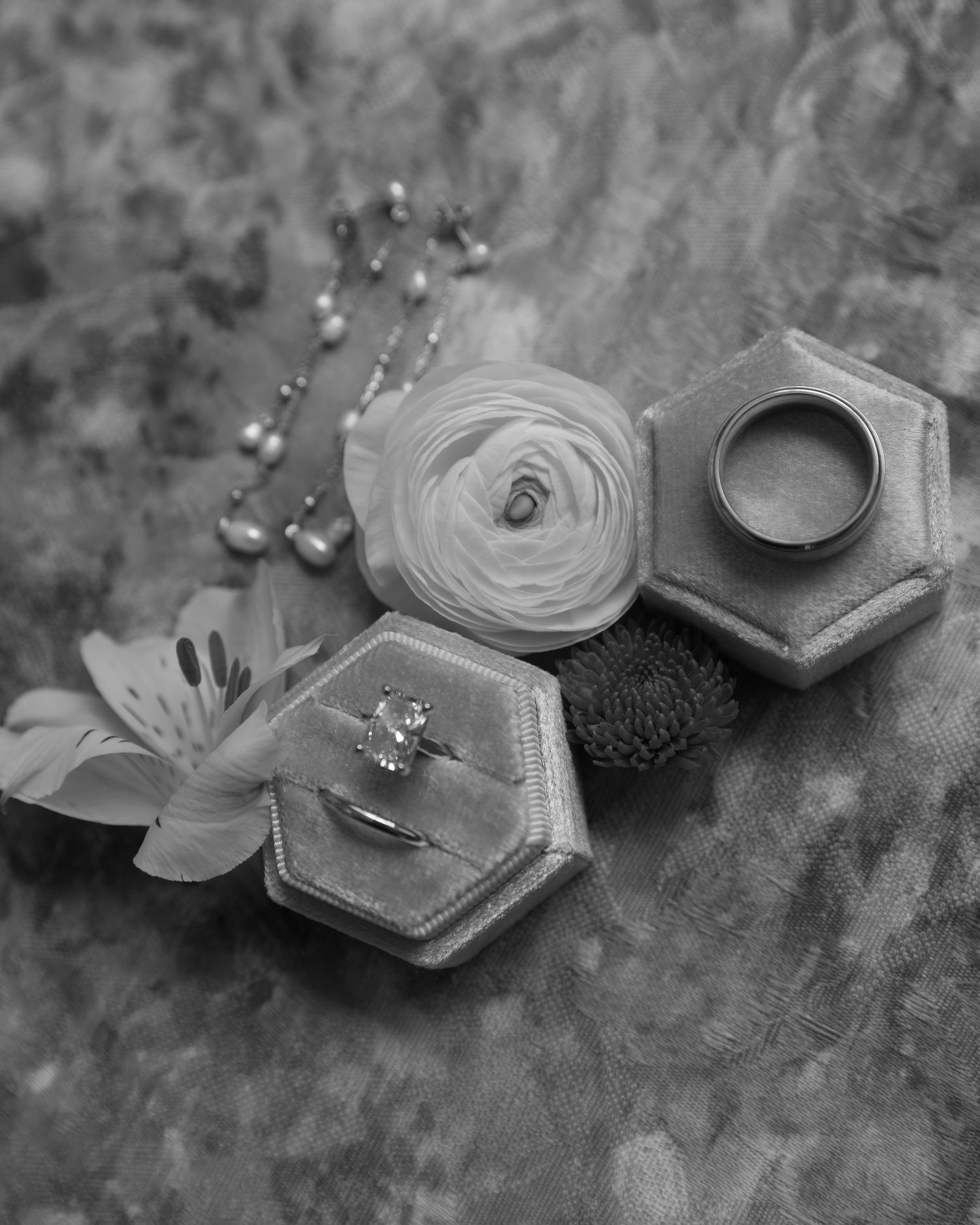 Black and white wedding ring detail photos arranged artistically on a textured surface with flowers.