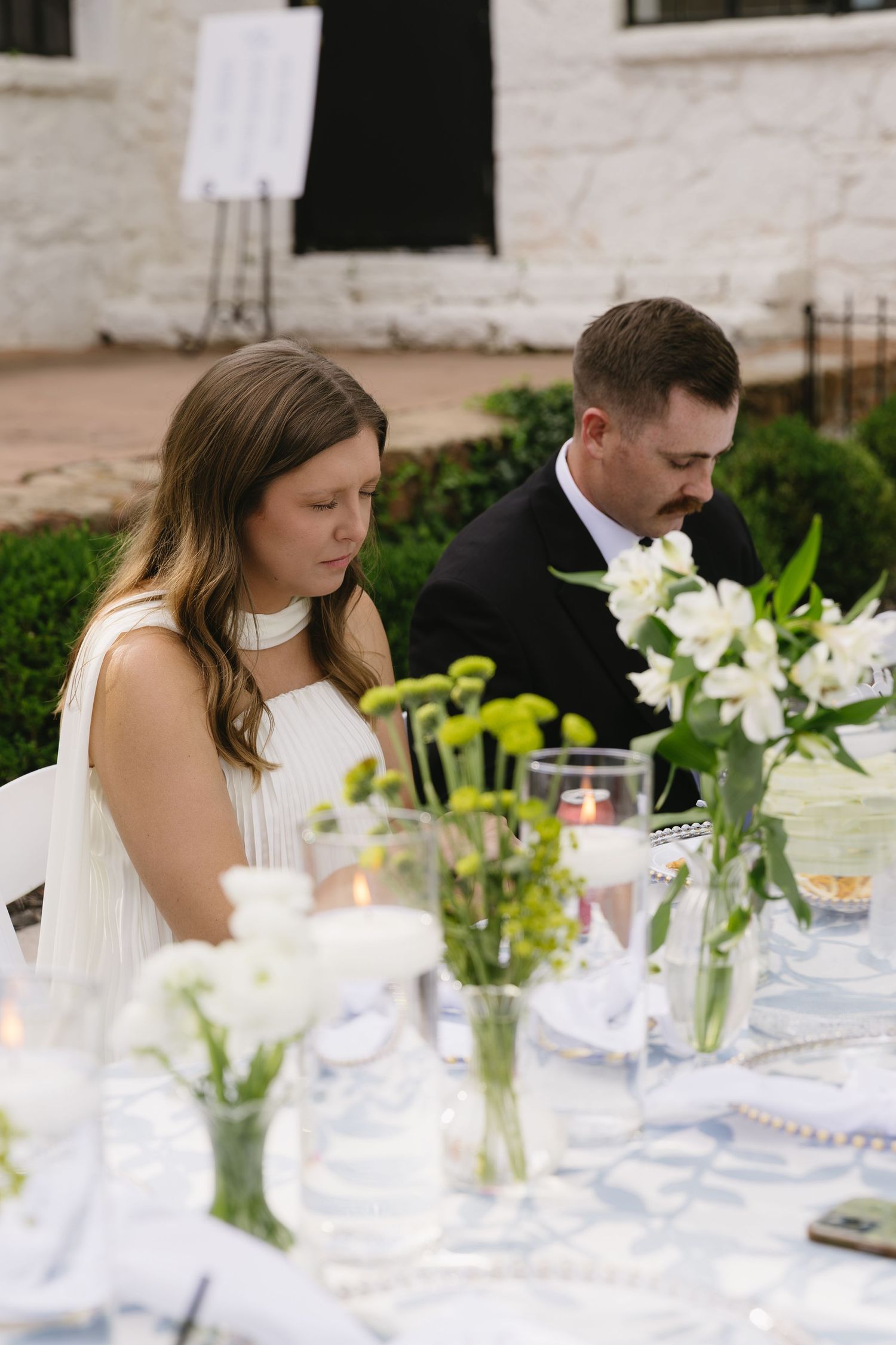 White floral table settings with candles create an elegant romantic outdoor dining atmosphere.
