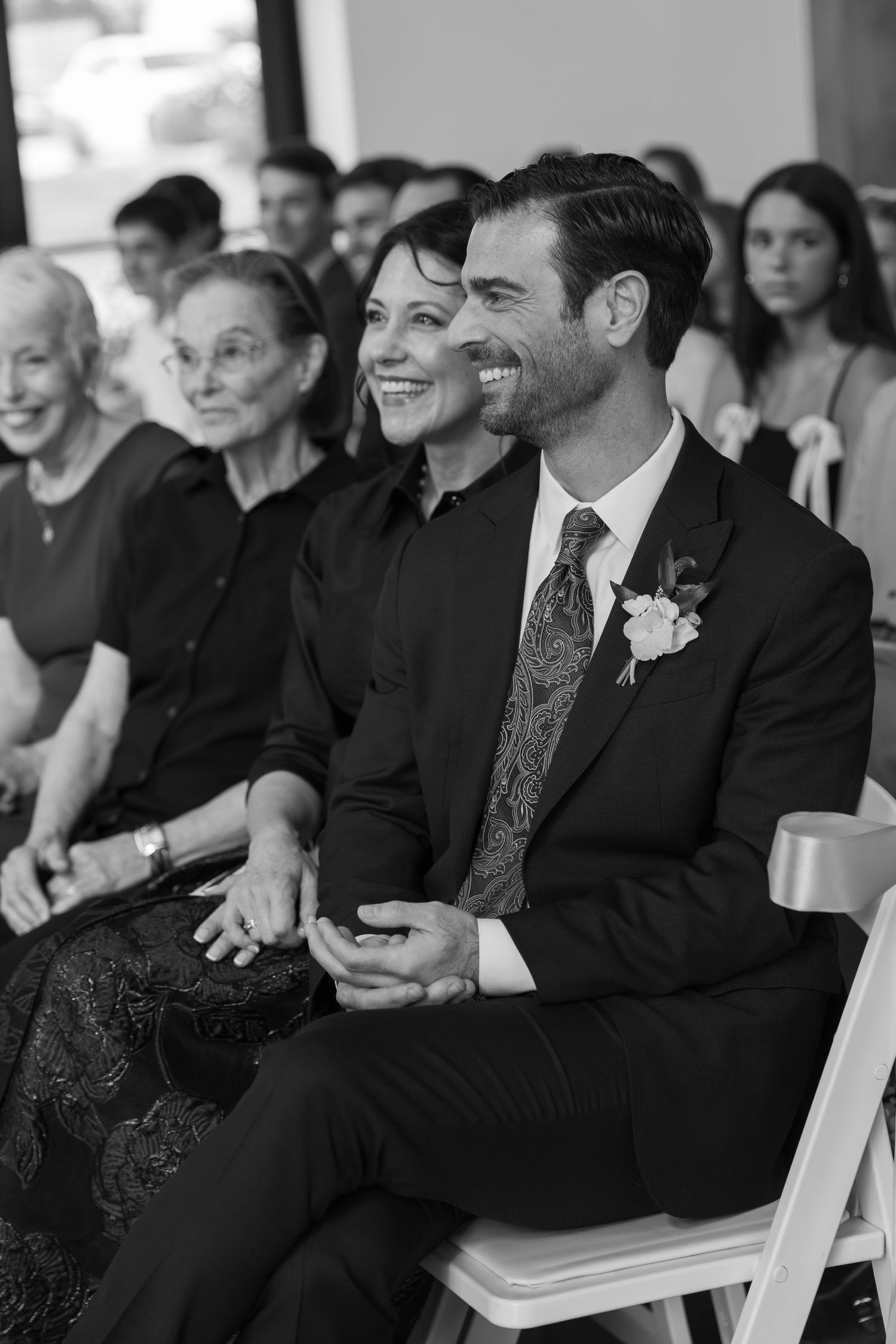 Wedding guests and audience members smile and laugh during a ceremony.