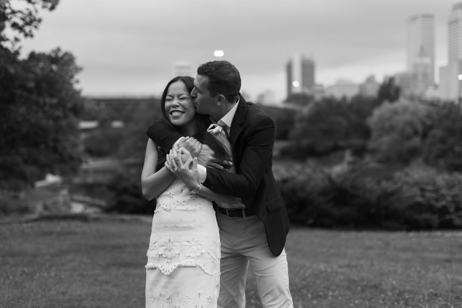 A tender romantic moment captured outdoors against a city skyline backdrop.