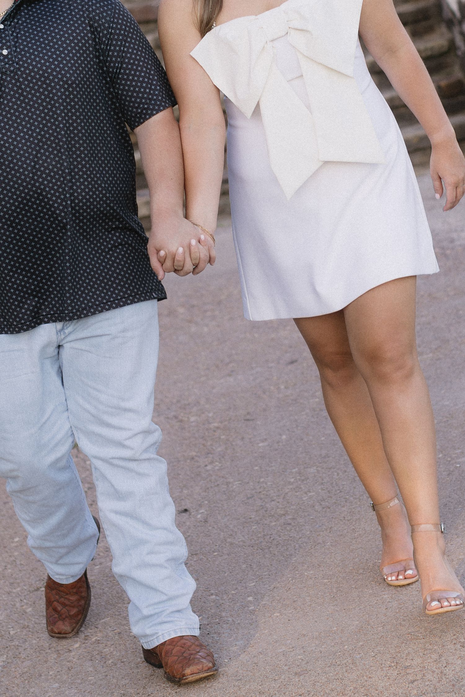 Close up view of couple's feet showing brown boots and white heels dancing or walking together on pavement.