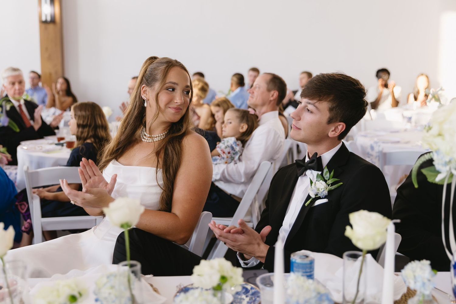 Wedding reception guests seated at tables enjoying a celebration in an elegant white venue.