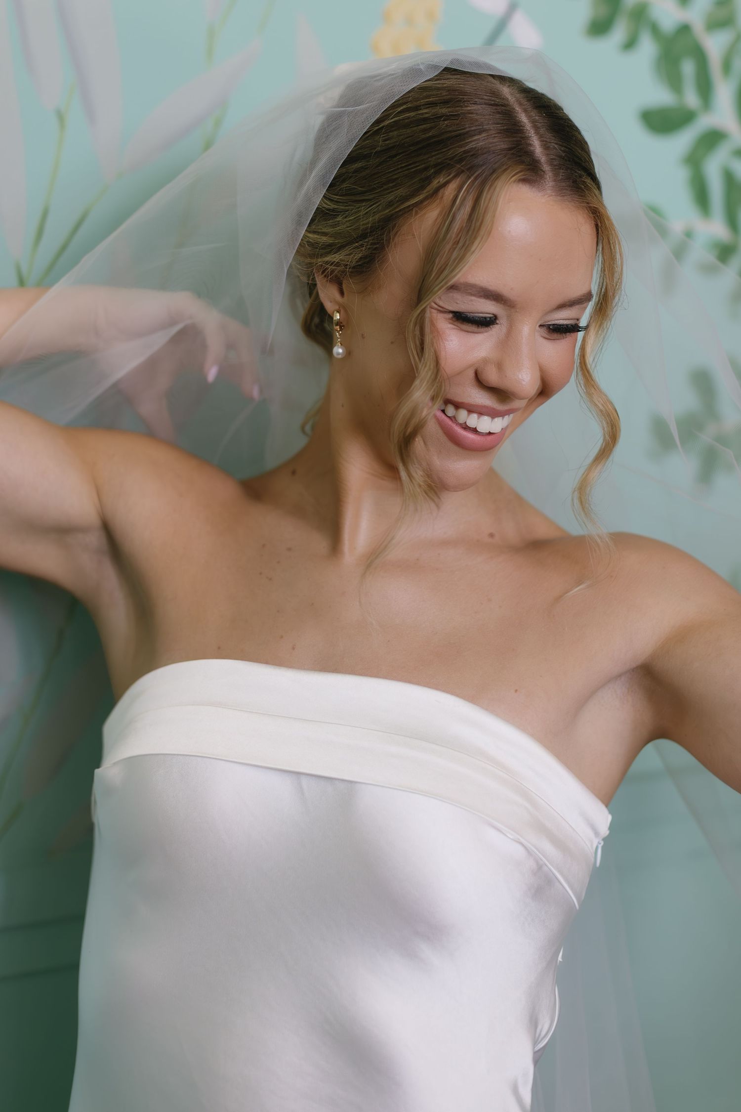 Close-up bridal portrait against turquoise wall showing off strapless neckline and joyful expression.
