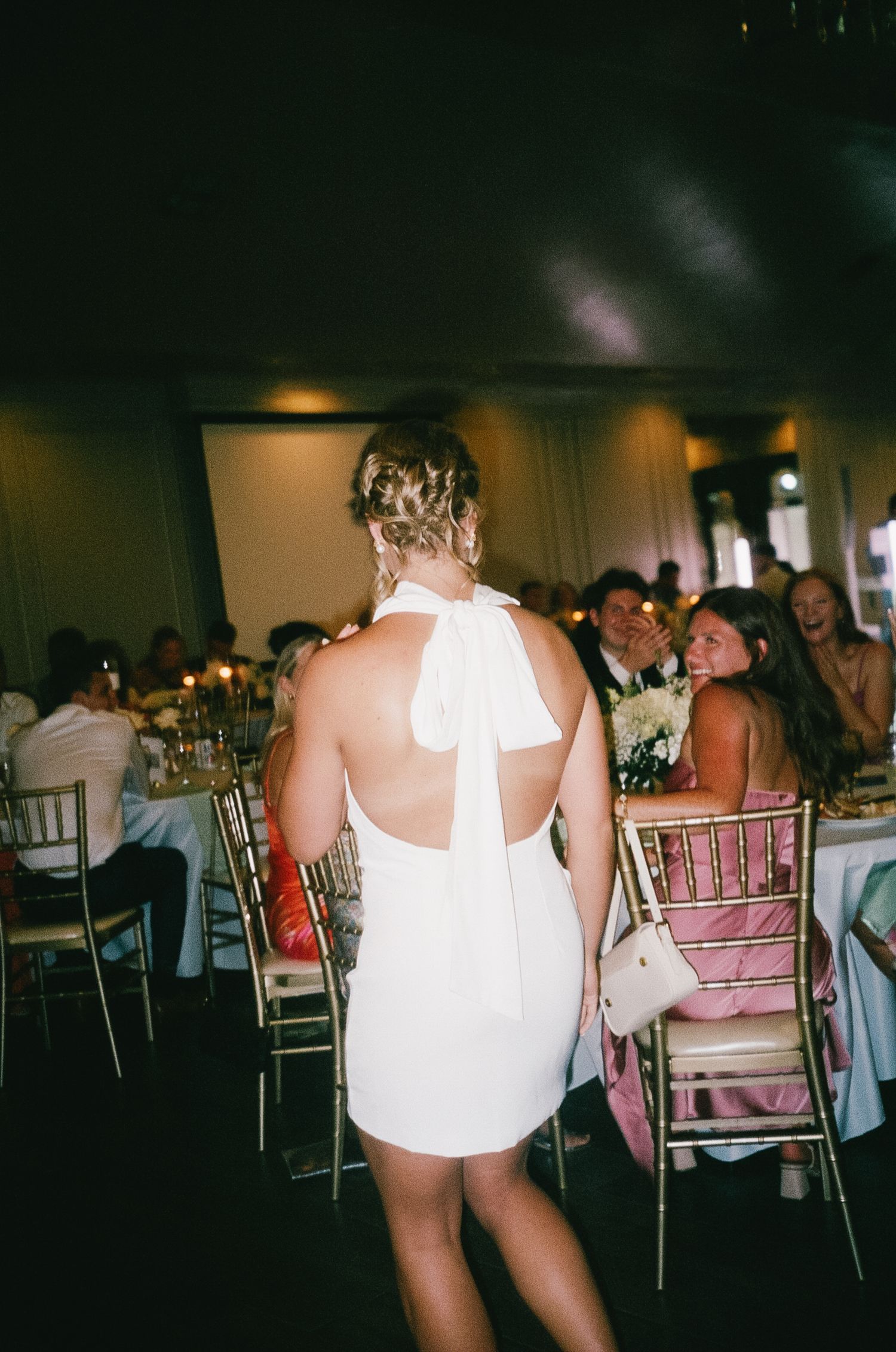 Guests sit at elegant tables during a wedding reception with decorative chiavari chairs.