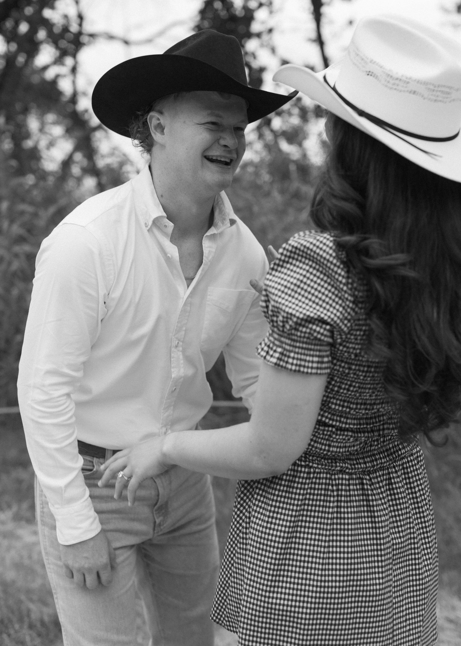 Couple in western attire shares playful moment wearing cowboy hats during outdoor photoshoot.