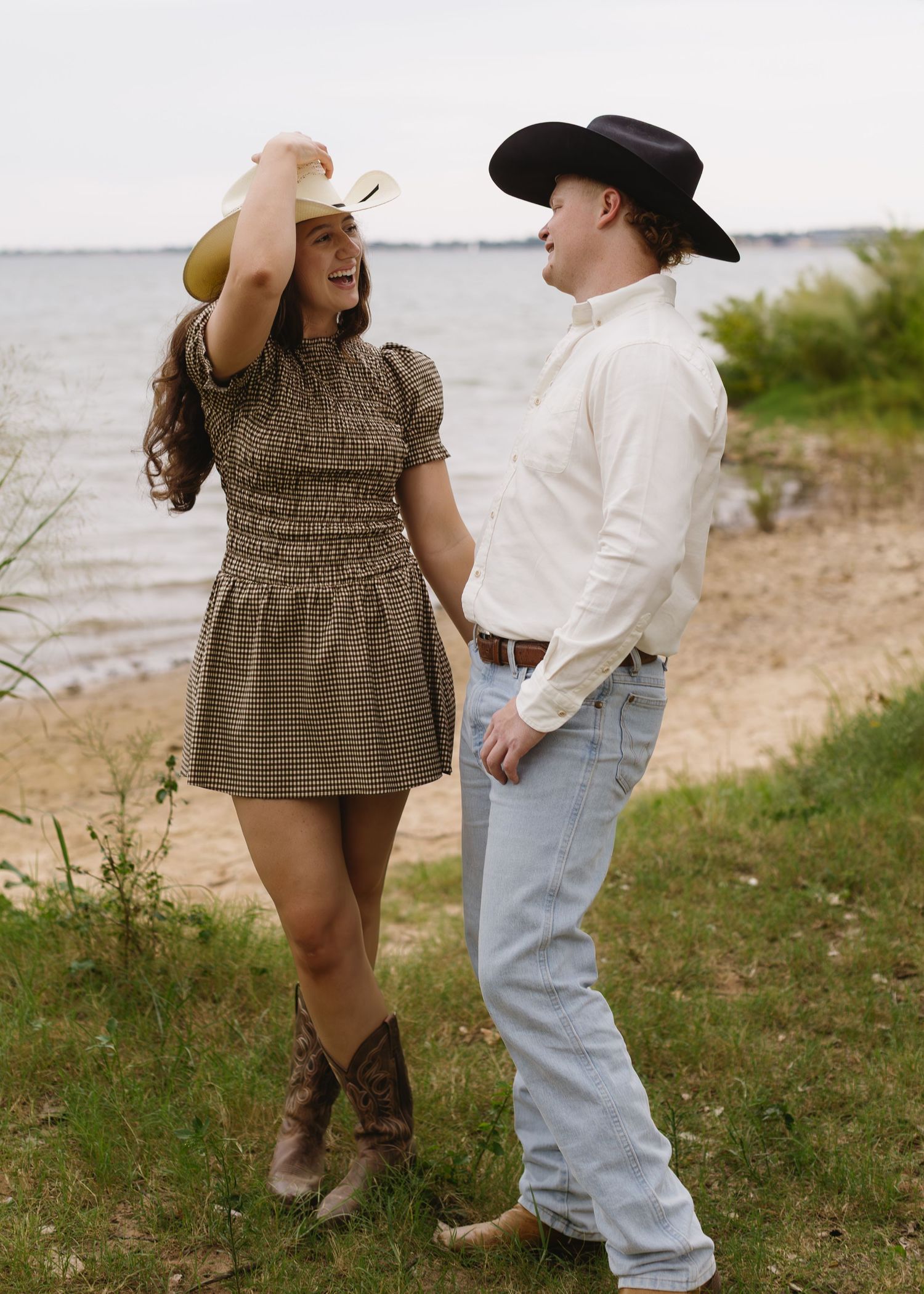 Couple in western-inspired outfits share tender moments by the waterfront.
