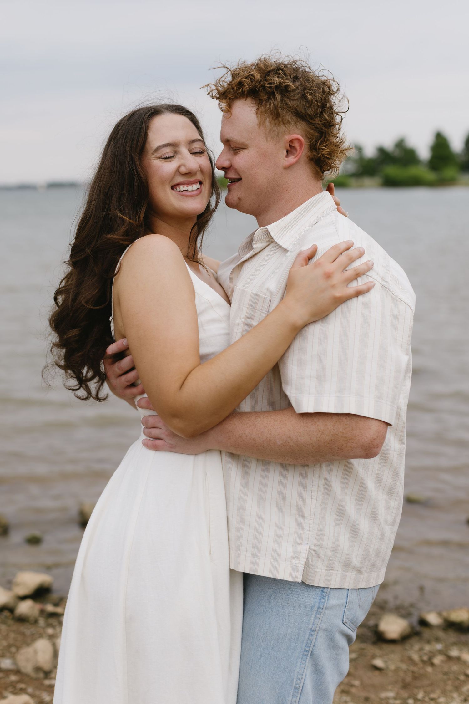 Happy couple laughs and embraces by the waterside during their romantic photoshoot.