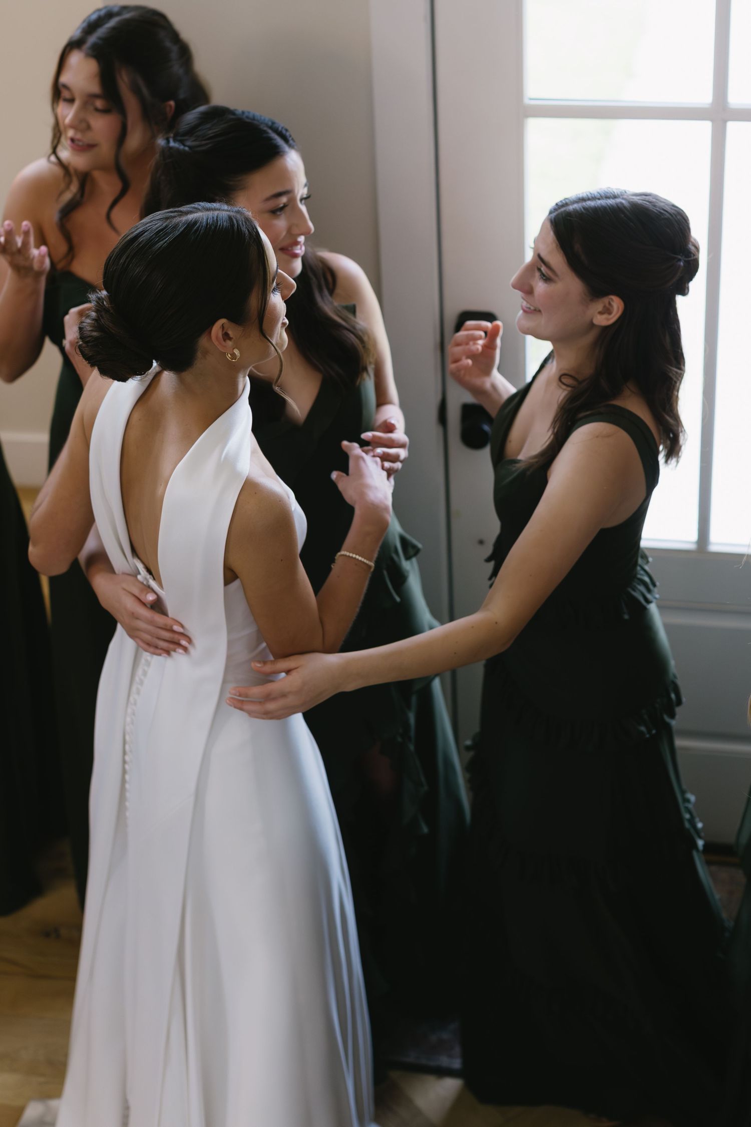 A wedding party gets ready indoors with attendants in black dresses helping with final preparations.