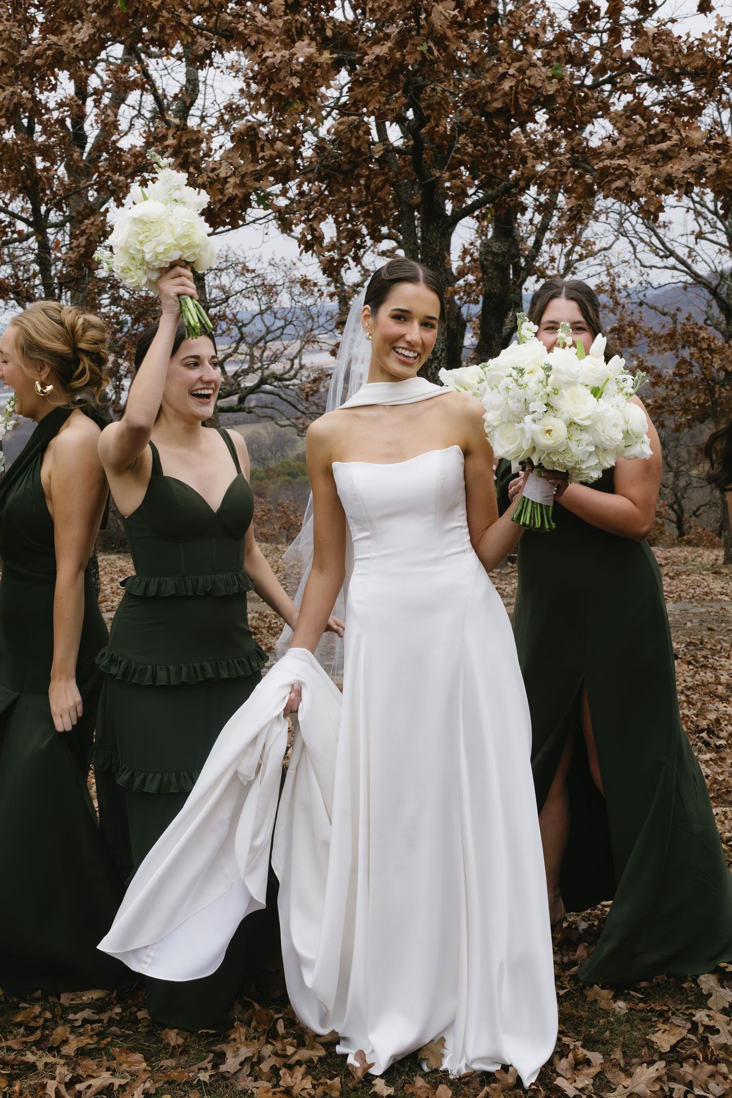 Wedding party poses outdoors with bridesmaids in black dresses and bride in white gown holding bouquets.