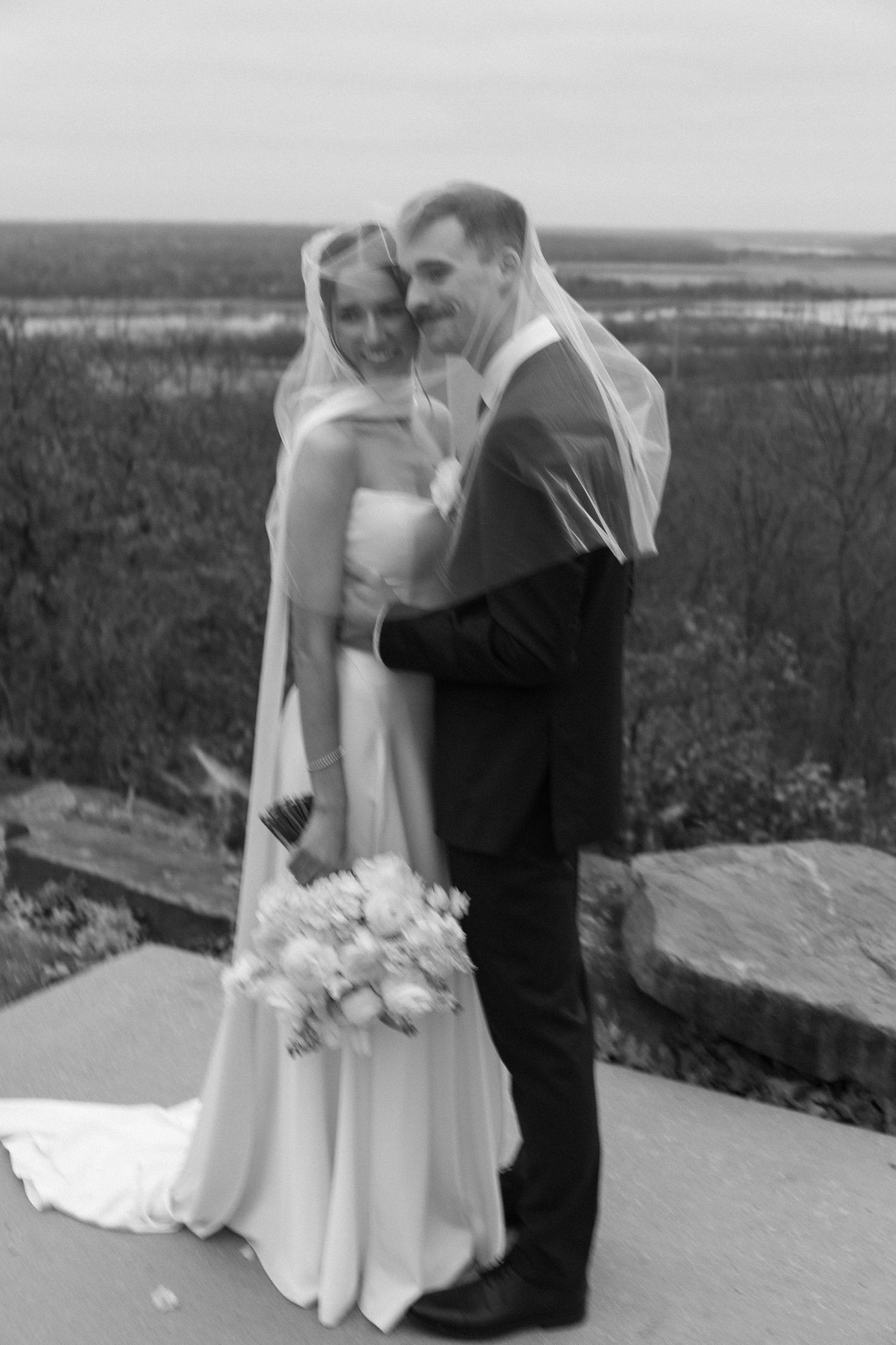 Couple sharing intimate moments during outdoor wedding photoshoot with scenic landscape backdrop.
