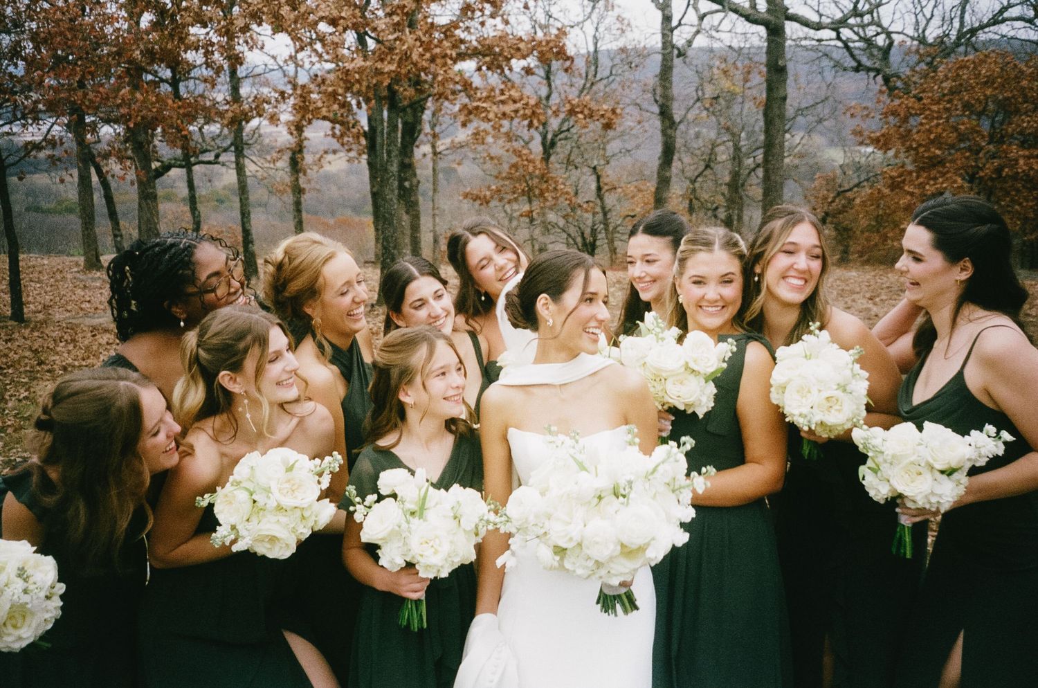 Wedding party poses with bouquets against an autumn landscape with fall foliage.