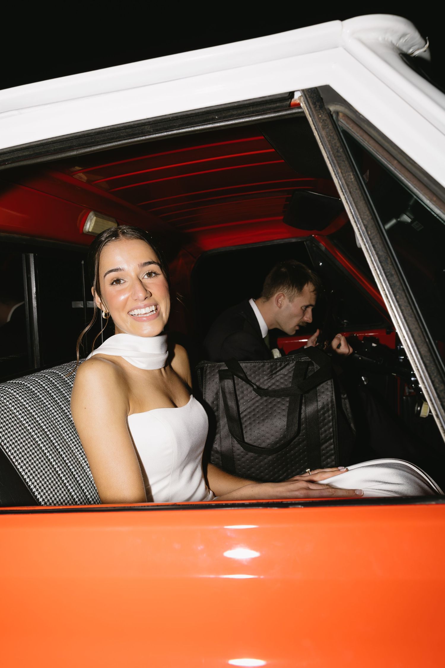 A vintage orange and white car with wedding decorations at night.