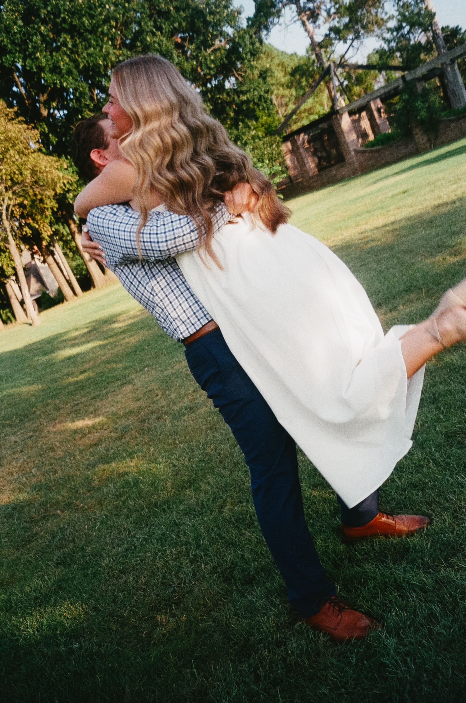 A couple embraces in a romantic dip pose on a sunny lawn with trees in the background.