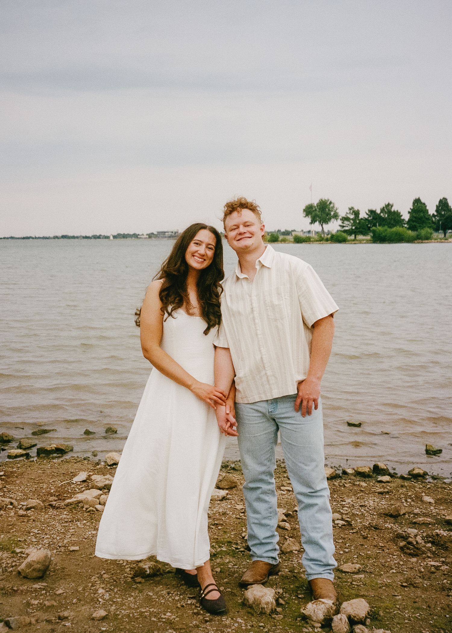 Couple enjoying a romantic stroll along a rocky shoreline at sunset by the calm waters.