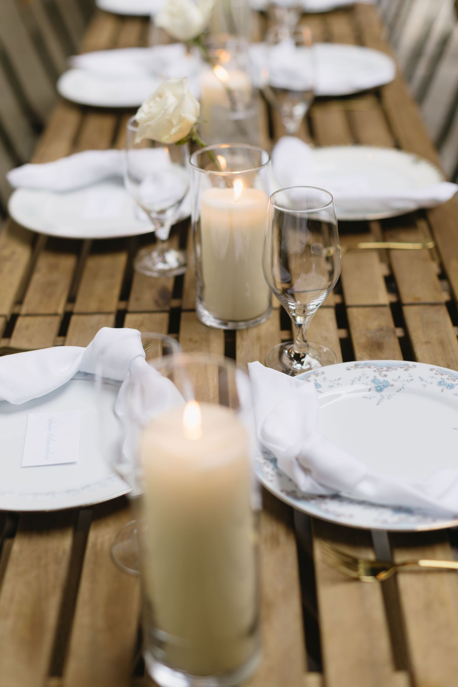 Close-up of white candles and place settings on wooden tables at a minimalist wedding reception.