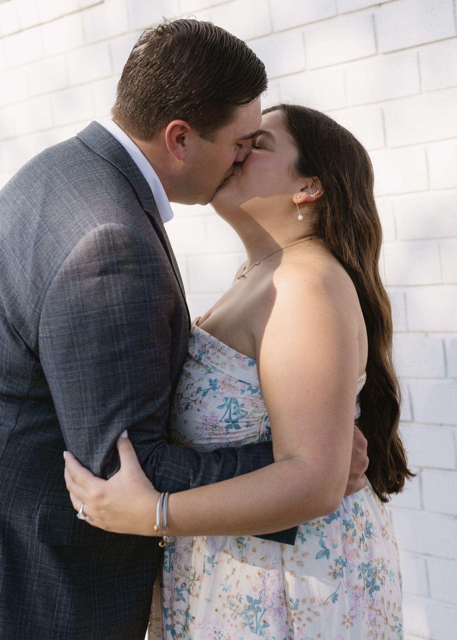 Intimate moments of a couple in formal attire against a white brick wall background.