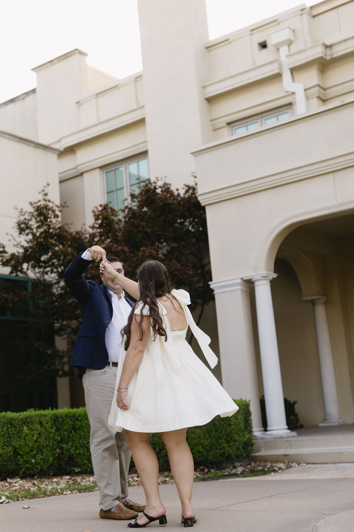 A couple dances and twirls together outside a columned building.