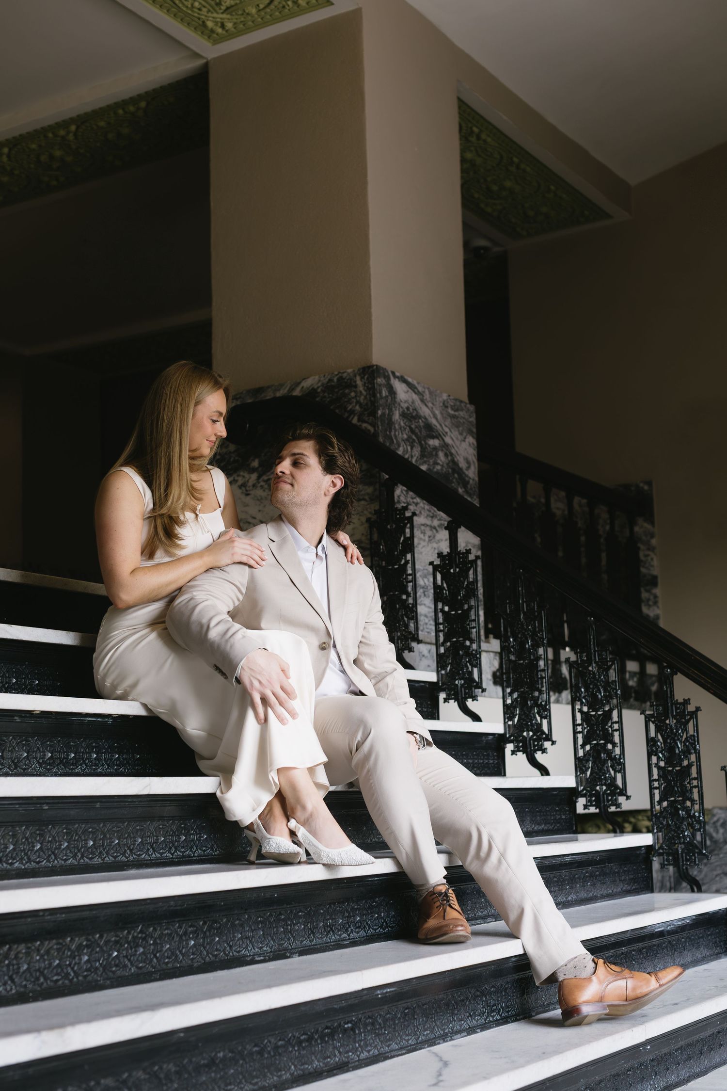 A couple relaxes together on grand interior steps with ornate railings.