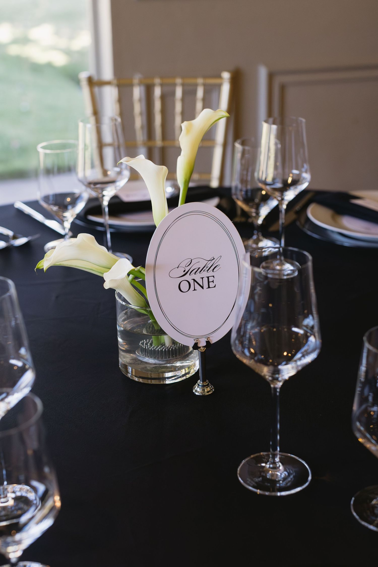 Elegant table setting with white calla lilies and wine glasses featuring a 'Table One' sign.