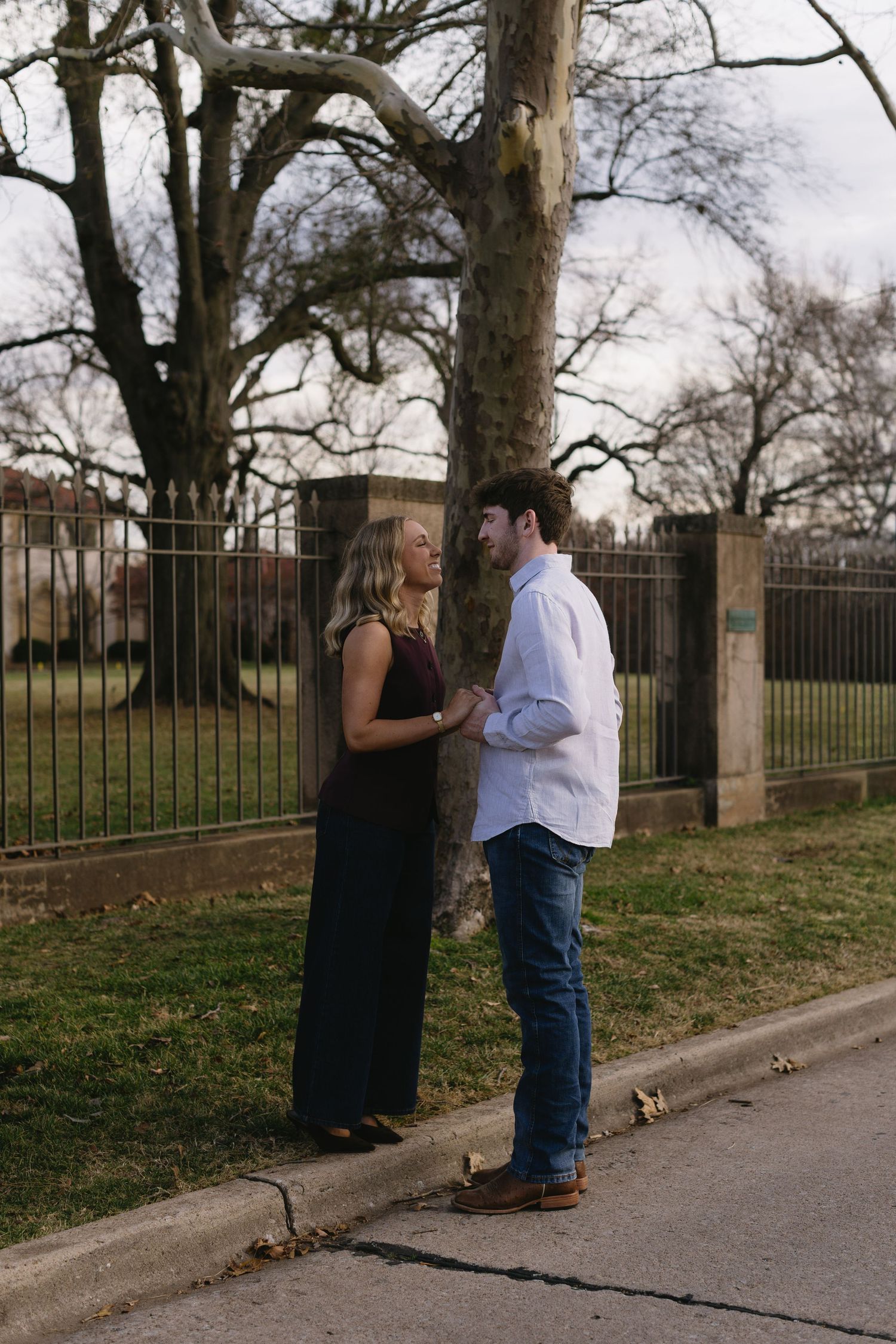 Romantic couple sharing an intimate moment outdoors by a fence and trees.