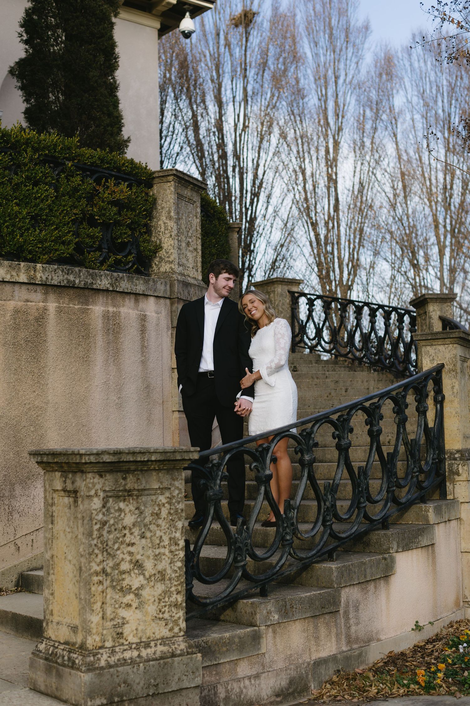 A couple poses on historic stone steps with decorative iron railings.
