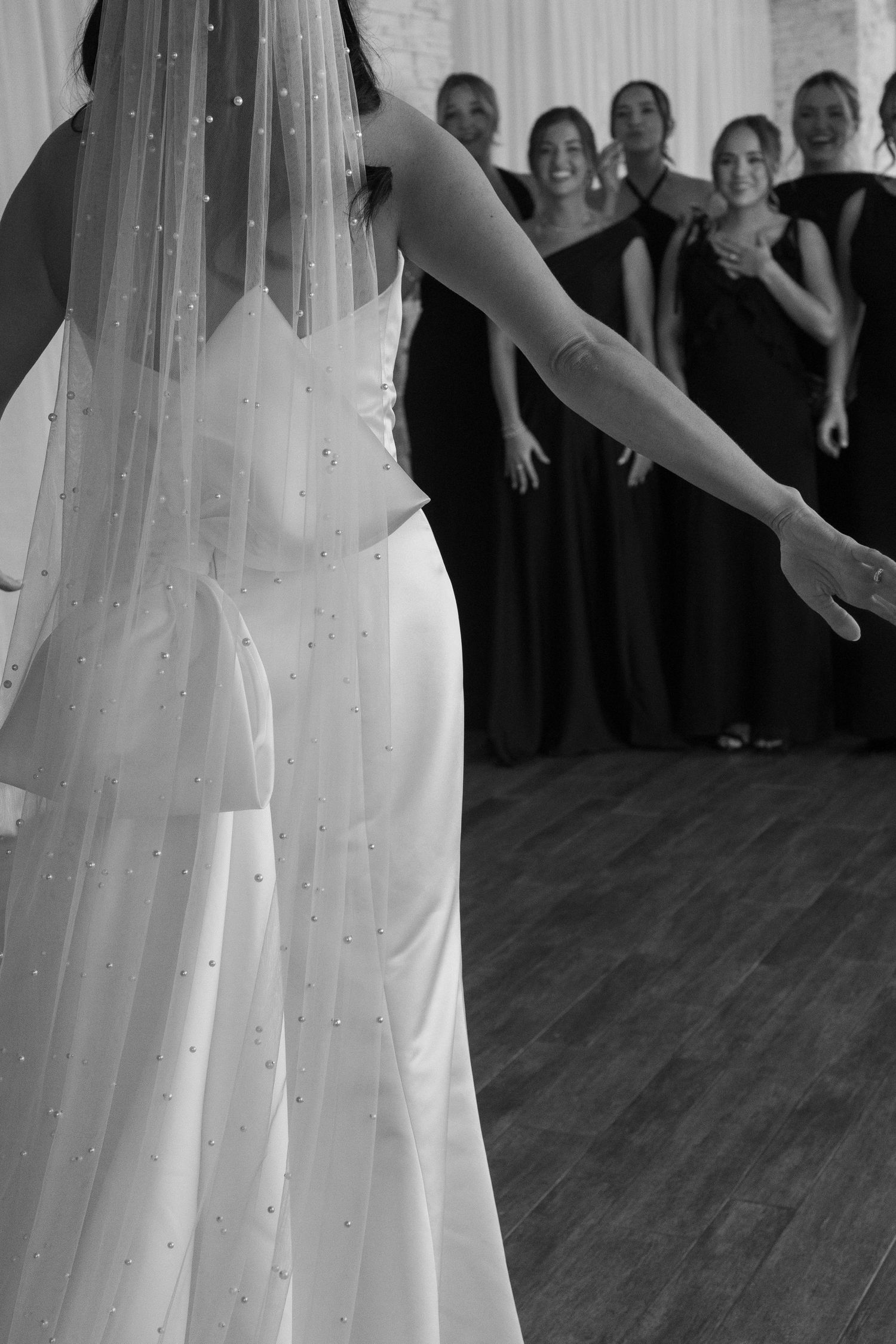 Wedding party watching bride in white gown and pearl-adorned veil.