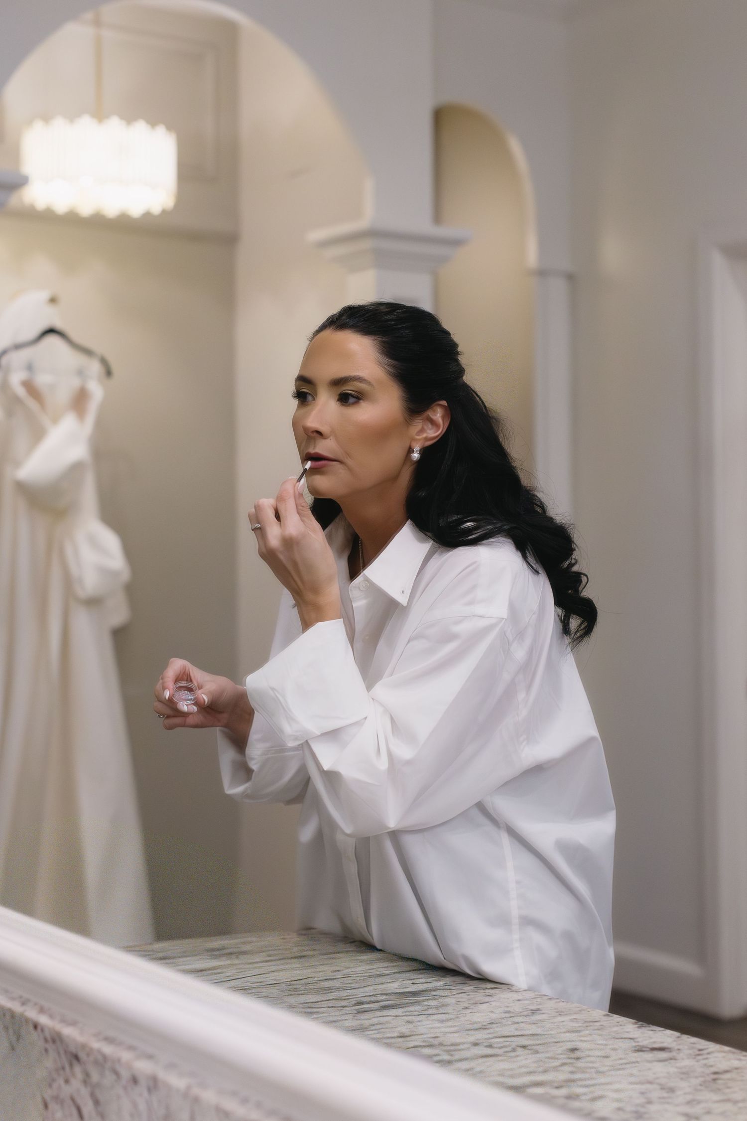 Bride in white robe getting ready for her wedding day in elegant dressing room with marble counter.