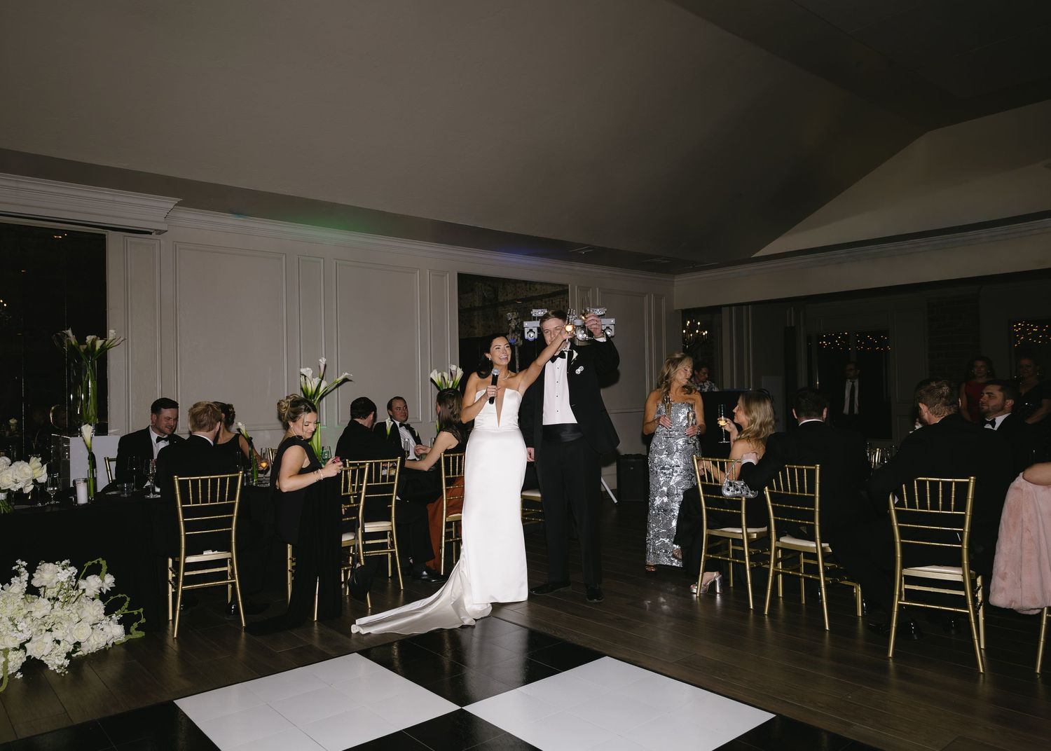 Wedding reception venue setup with gold chairs and dance floor in dark lighting.