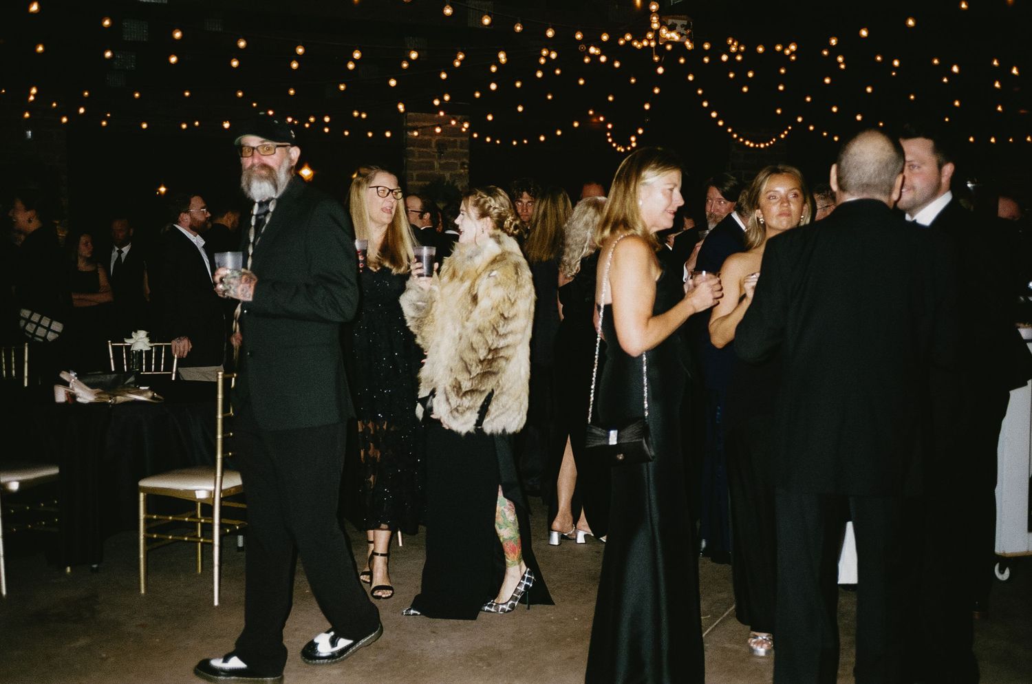 Wedding reception guests mingling and dancing under string lights.