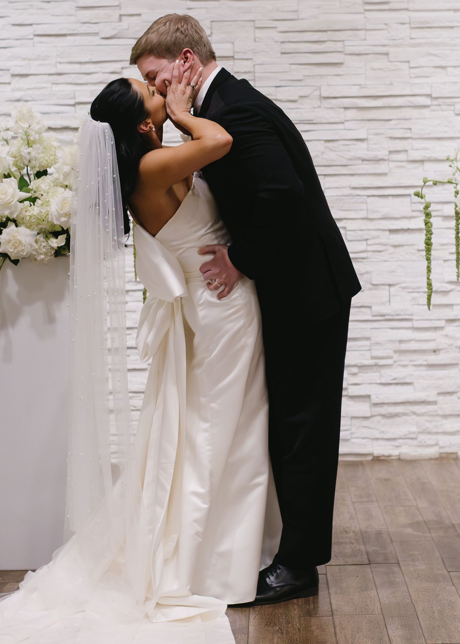 Intimate wedding kiss moment against textured white stone wall.