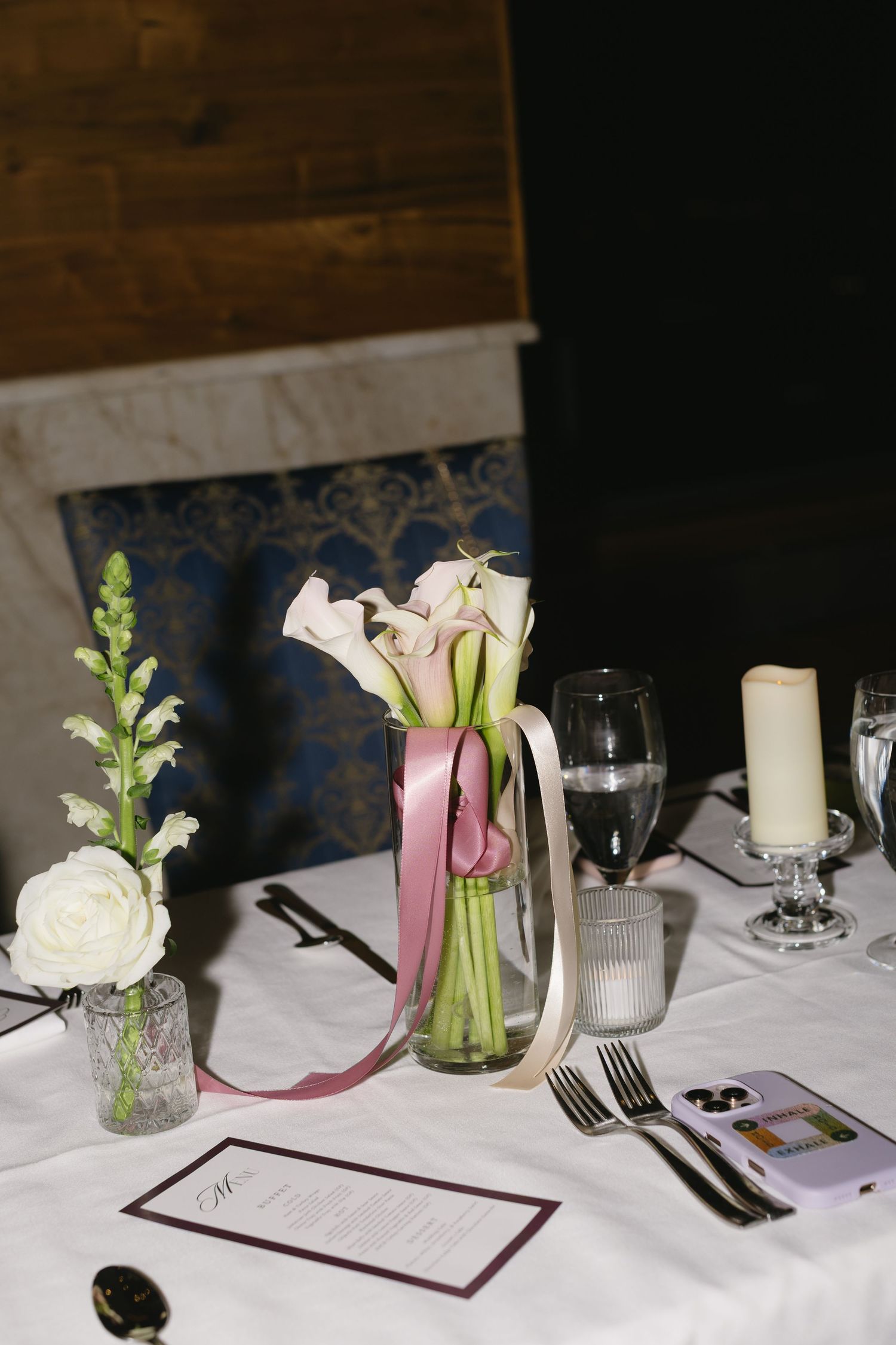 Elegant table settings with white flowers in glass vases, burgundy accents, and white linens at a formal event.