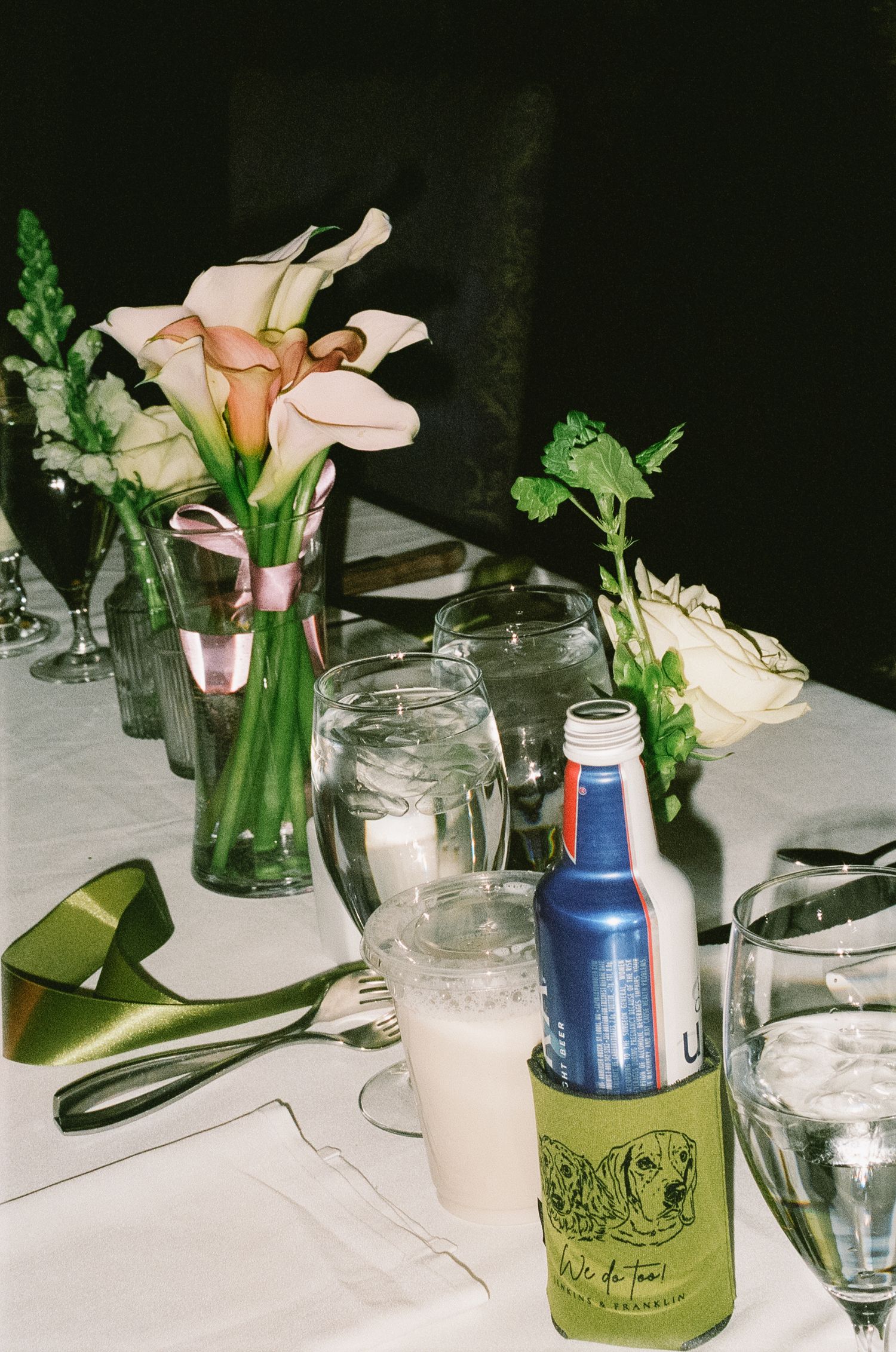 Wedding reception table decor with pink calla lilies in glass vases and scattered green accents.