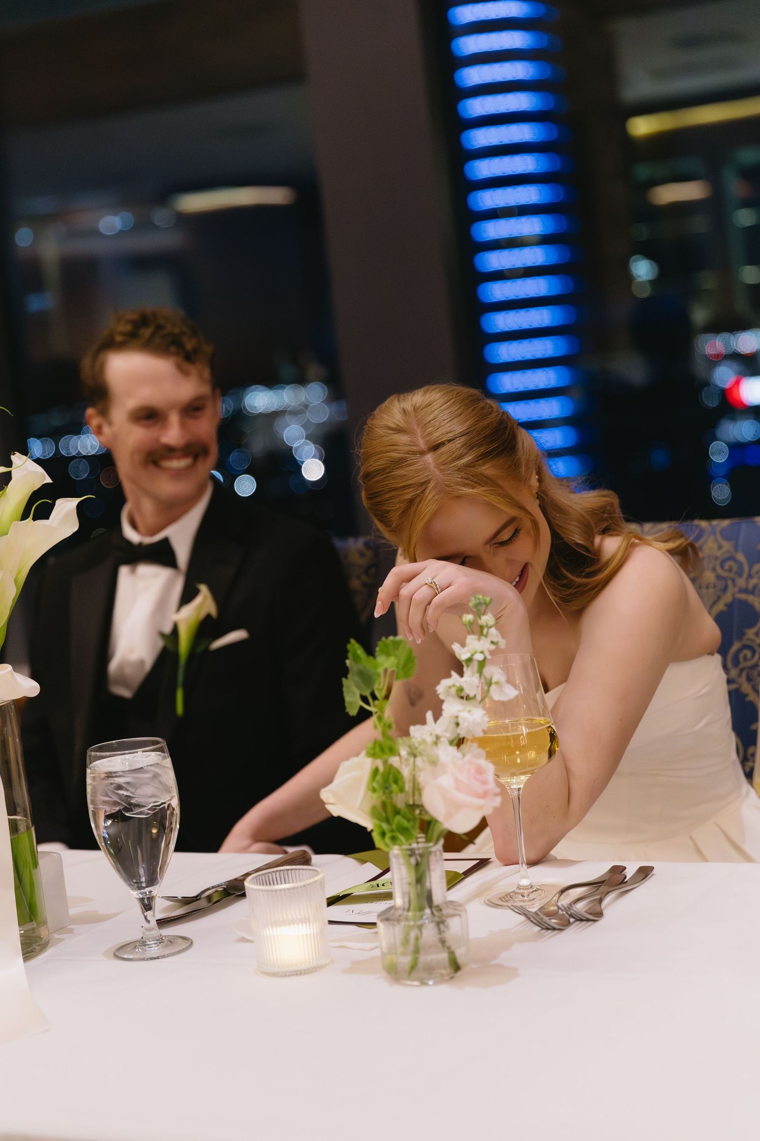 An elegant wedding reception table setting with white linens and floral centerpieces.