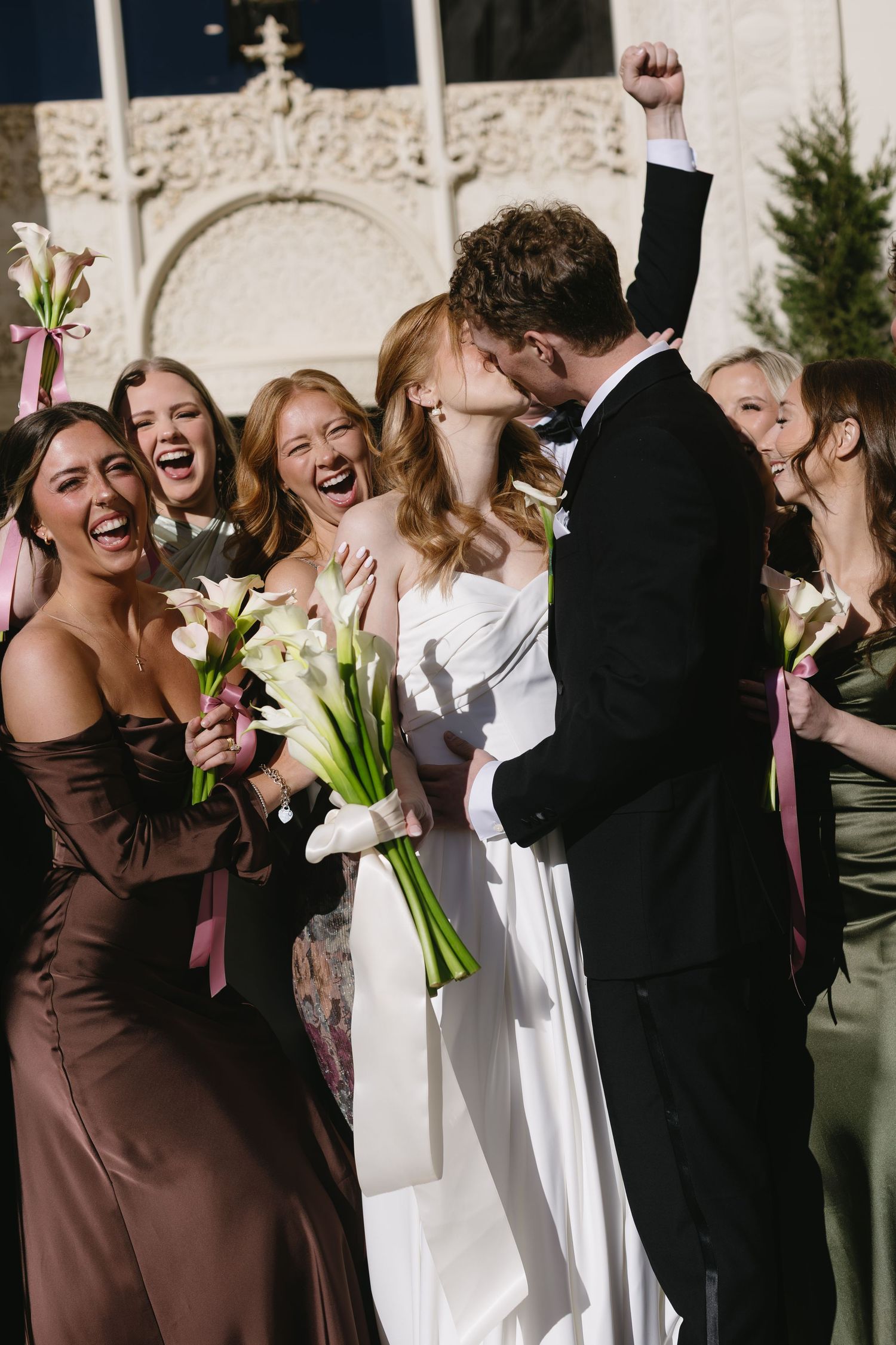 Wedding party celebrates with laughter and joy as the newlyweds share a romantic moment.