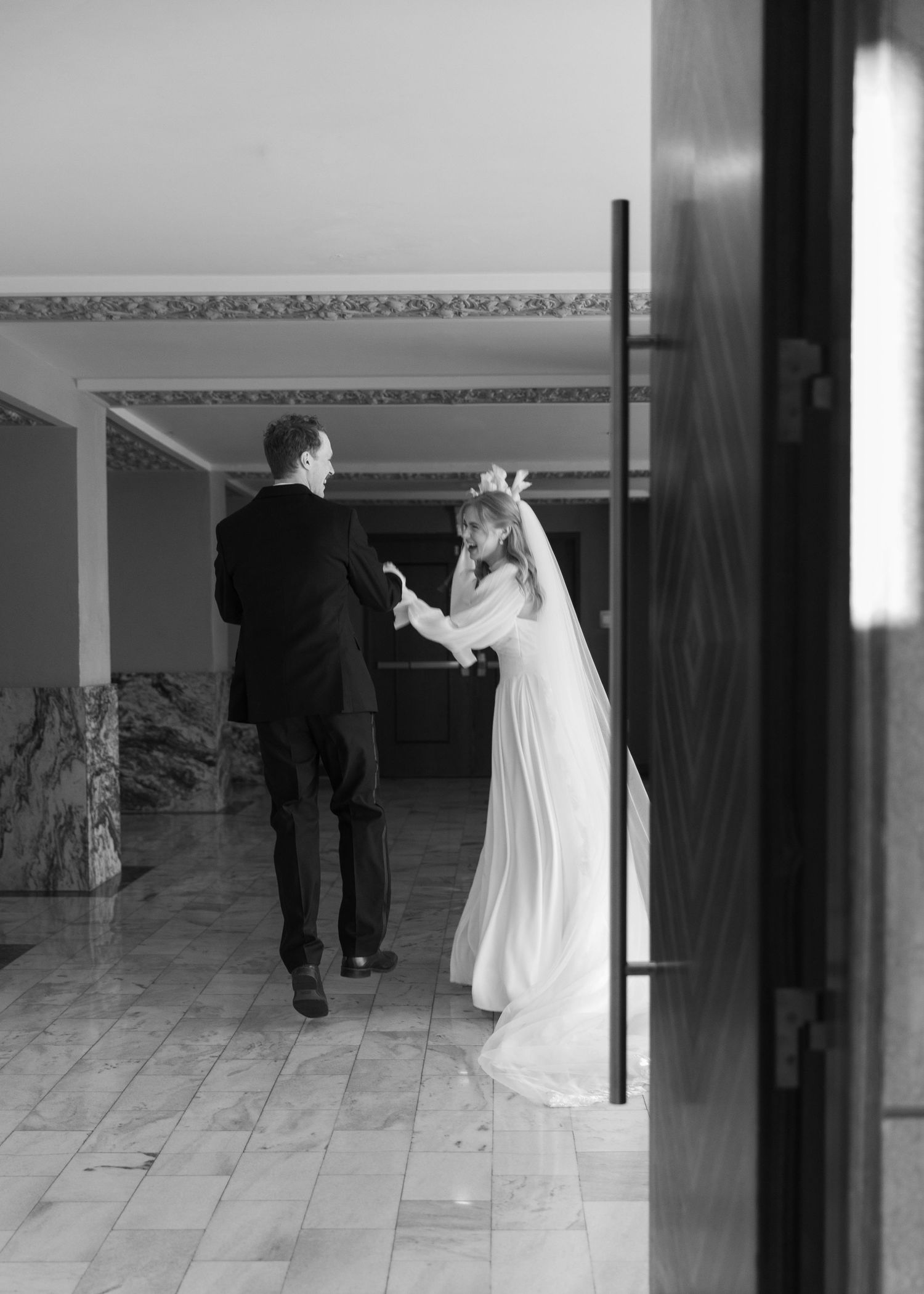Wedding couple dancing in an empty marble-floored ballroom with dramatic lighting.