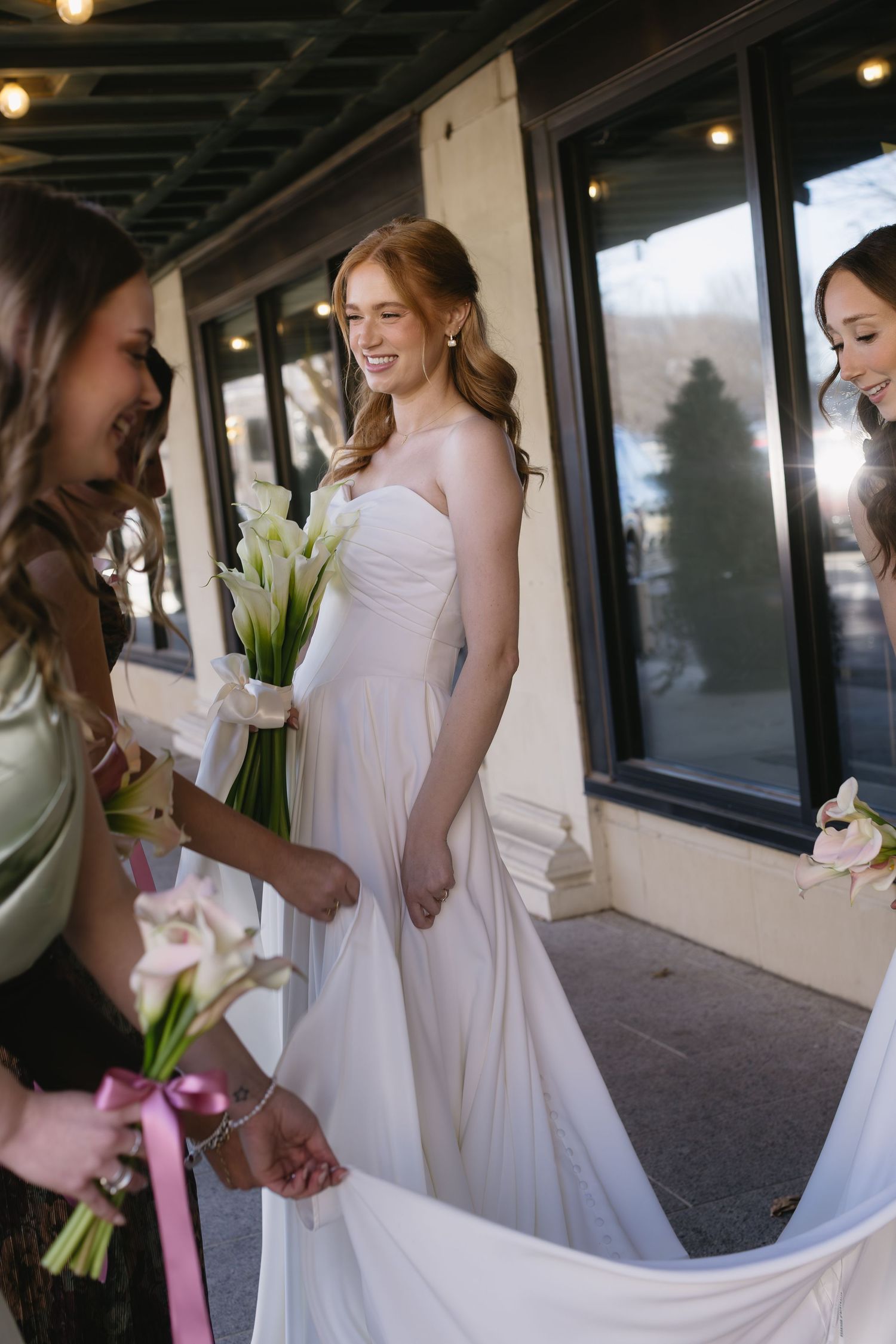 Bridesmaids in white dresses holding calla lily bouquets with pink ribbons.