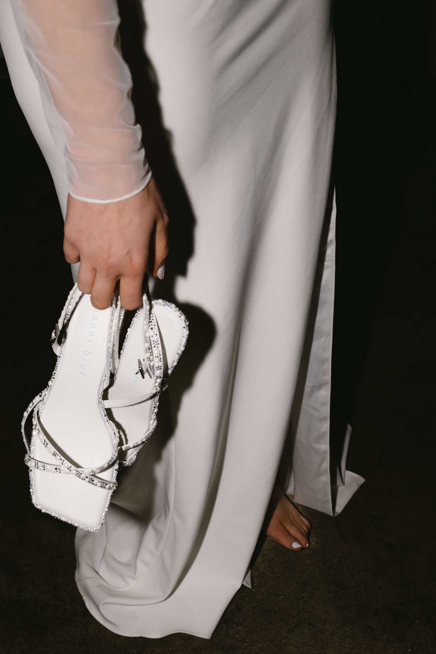 Close-up of a white wedding dress and shoes being held against a dark background.