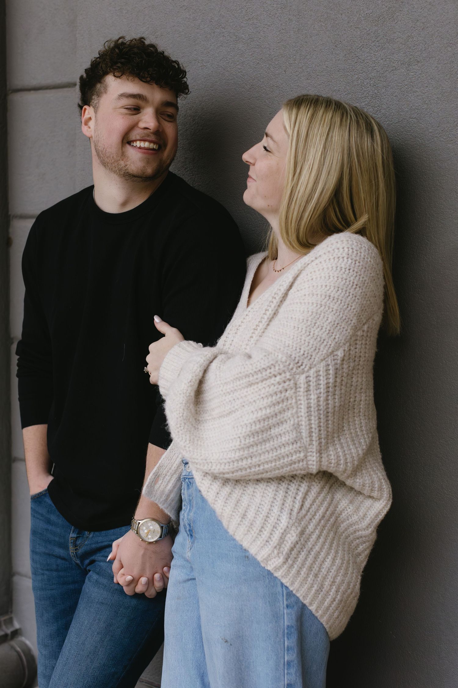 Two people share intimate moments against a grey wall in a series of candid shots.
