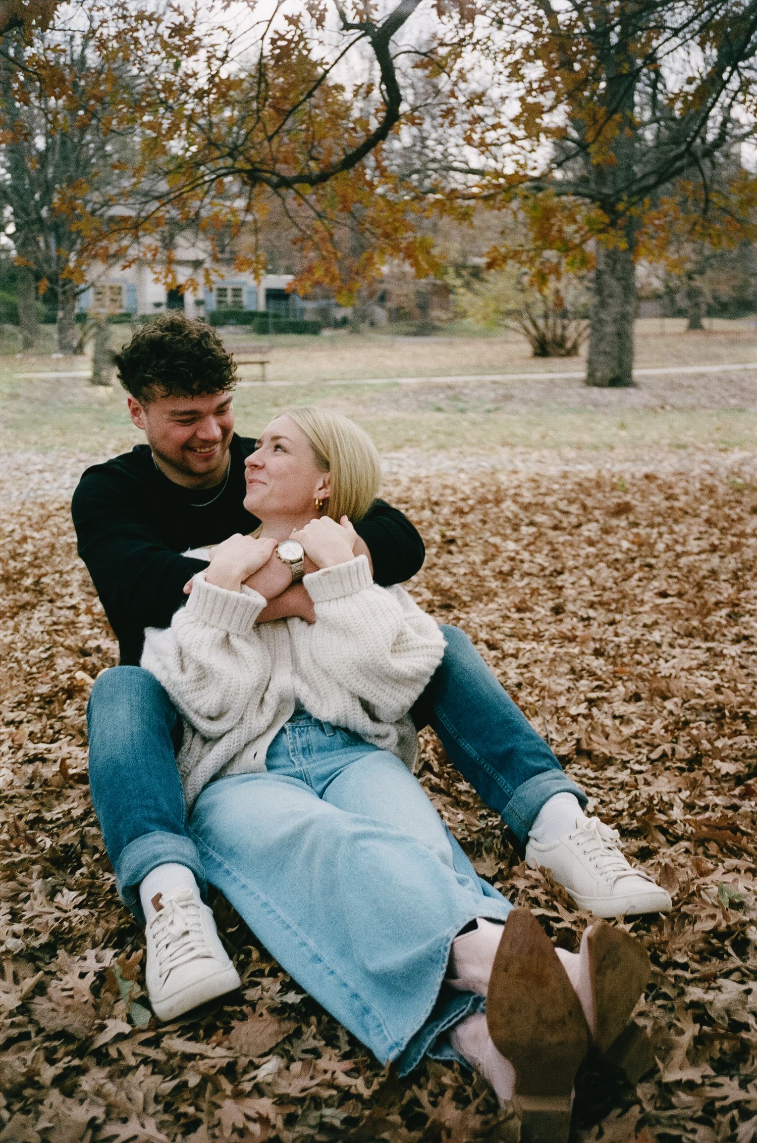 Couple lounging on fallen autumn leaves in coordinated casual outfits.