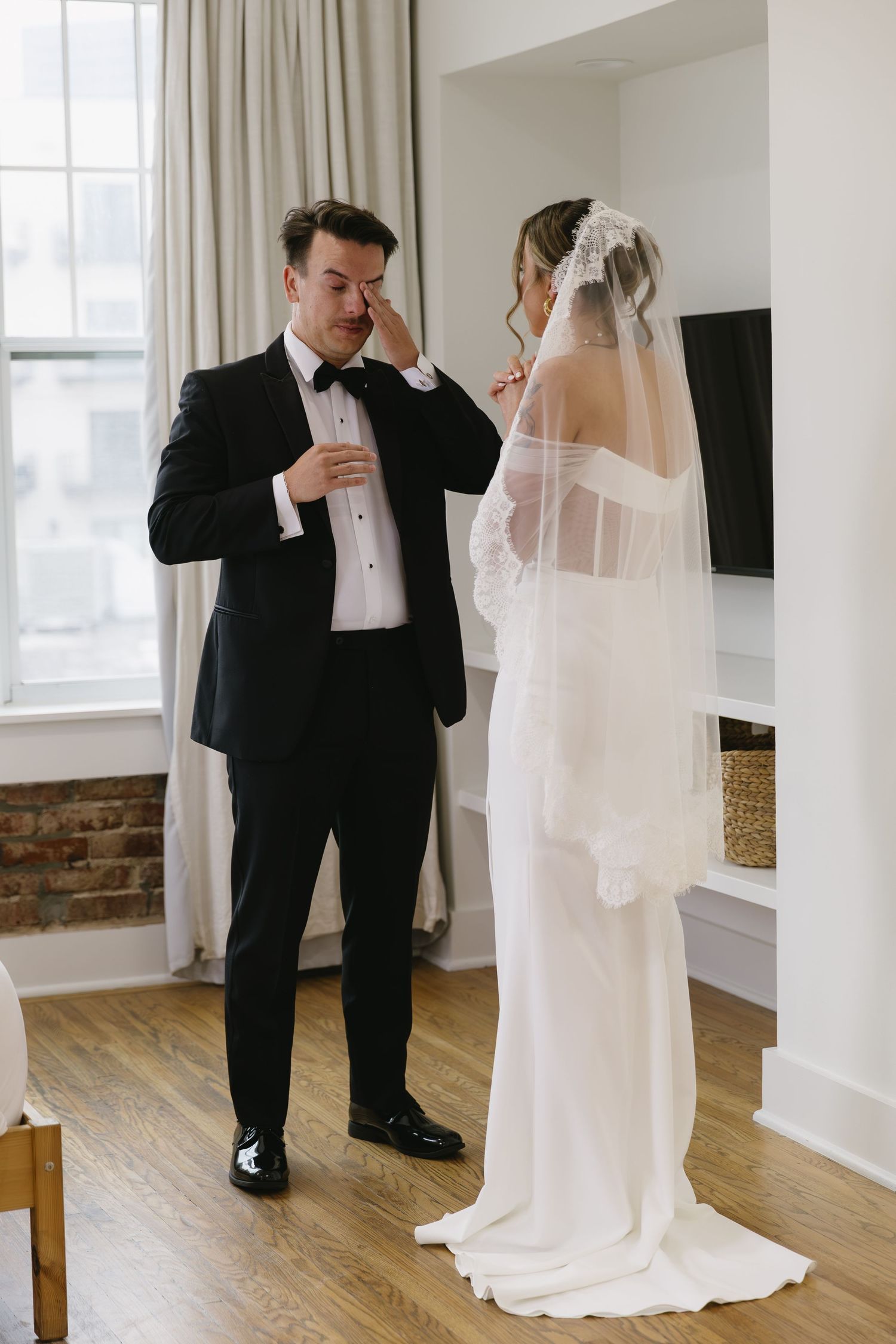 Bride and groom share a private moment in an elegant room with hardwood floors and white walls.