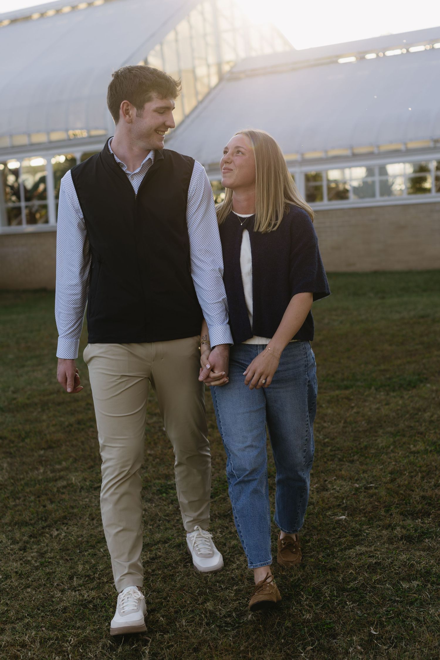 A couple in casual attire walks together on grass, with focus on their legs and lower bodies in a candid moment.
