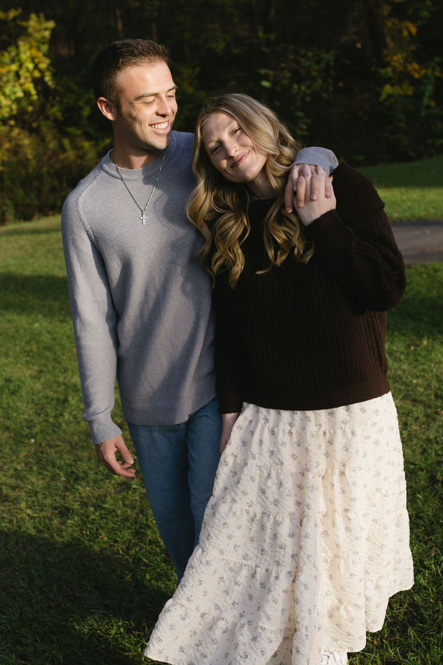 A couple laughs together outdoors wearing contrasting black and grey outfits.