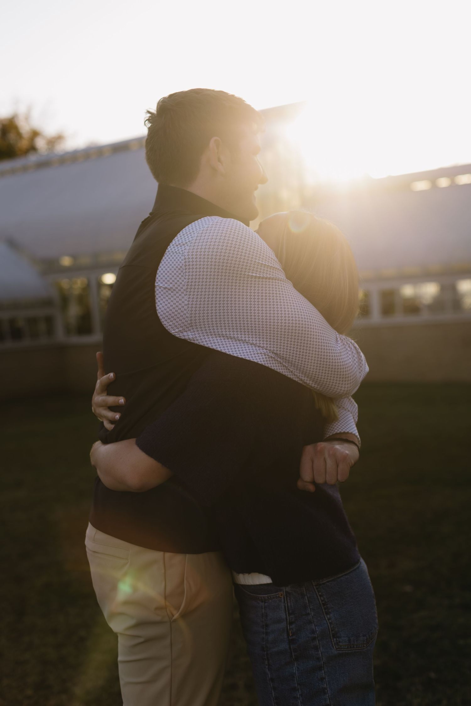 Two people sharing a warm embrace in front of a building during golden hour sunset.