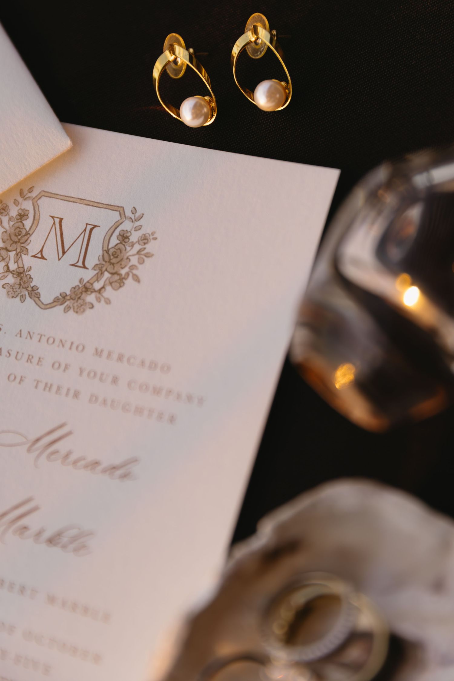 Elegant wedding invitation with gold monogram and rings photographed in soft lighting.