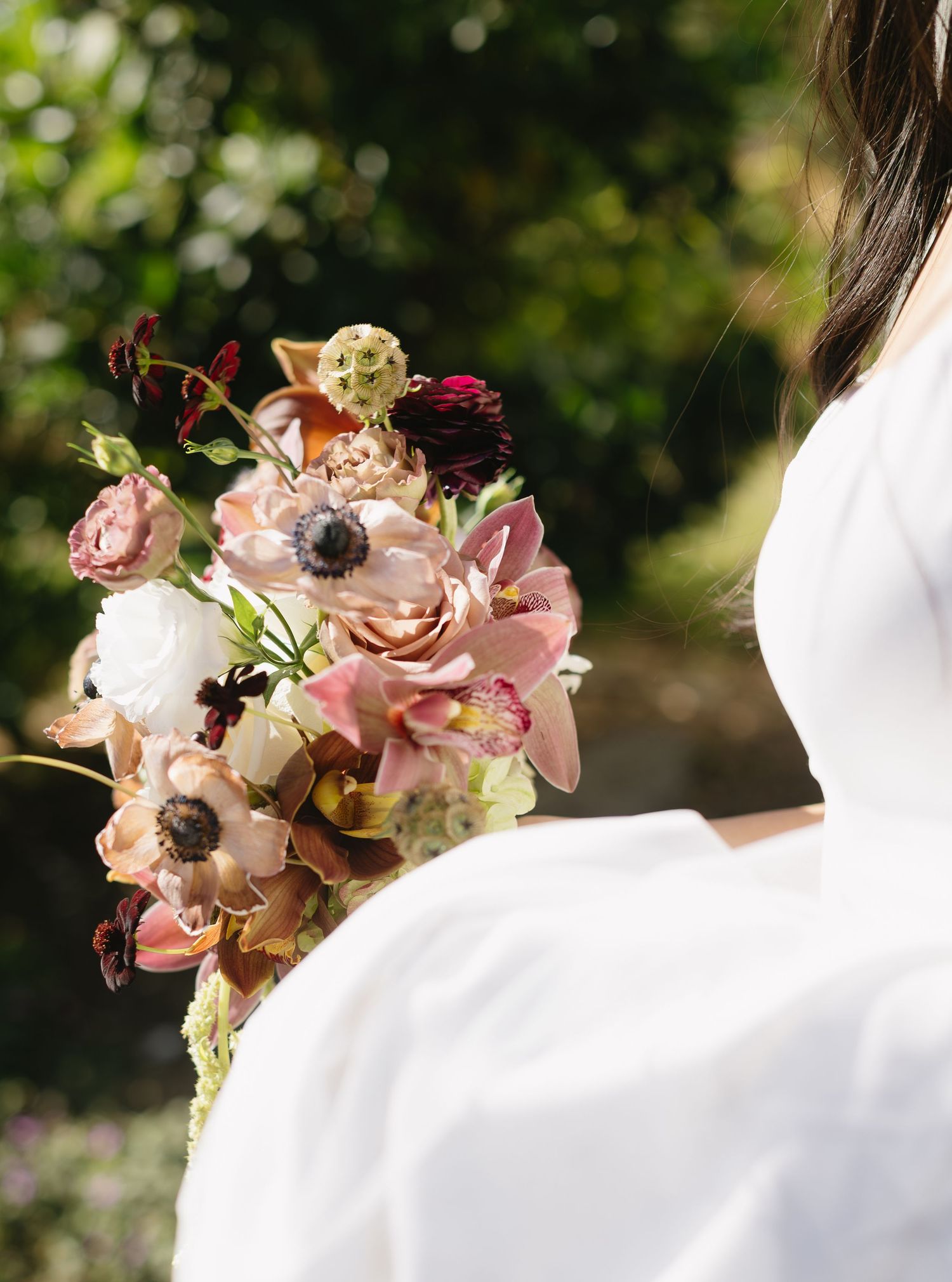 Elegant wedding bouquet with pink and white flowers against a white dress in sunlight.