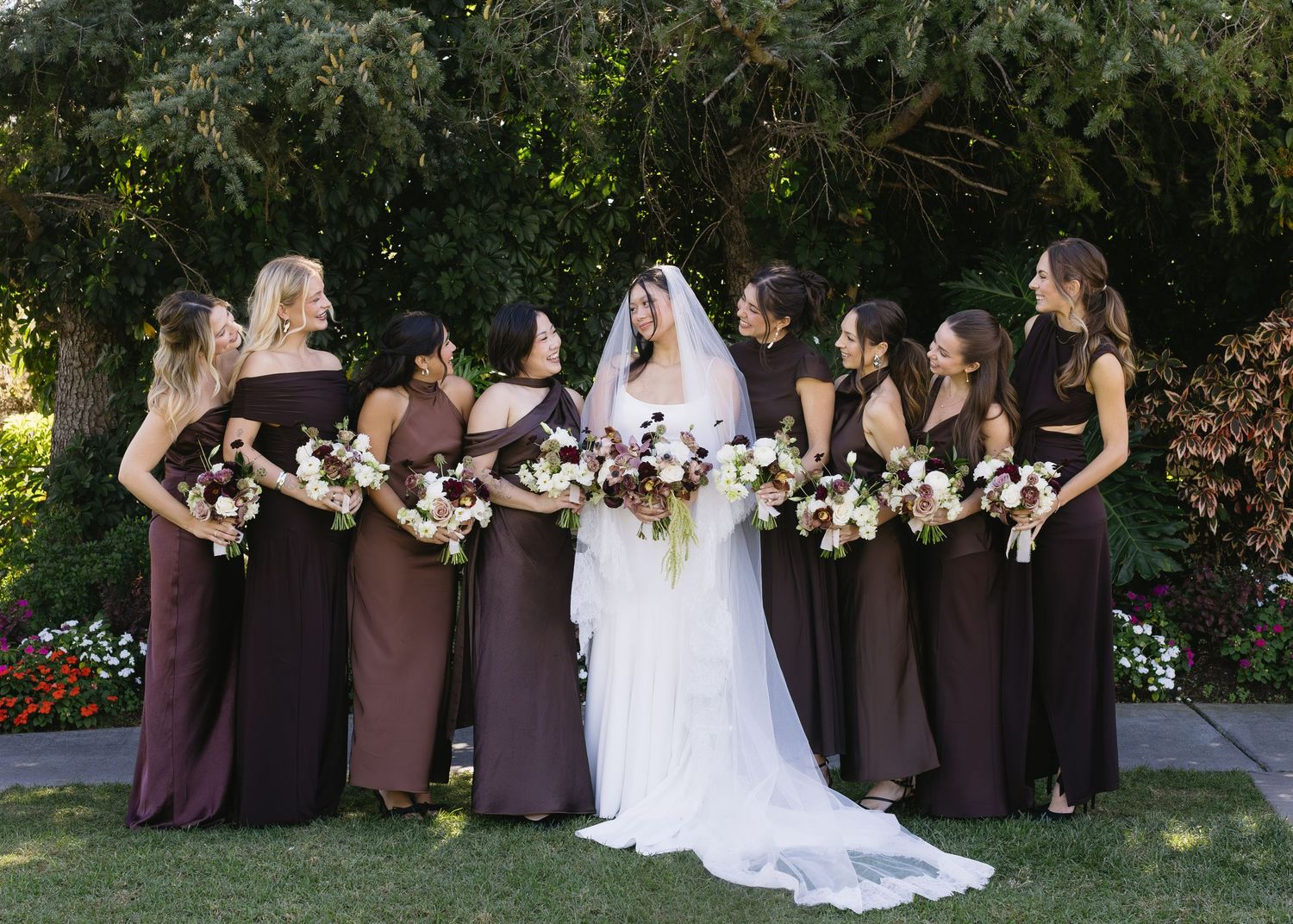 Wedding party in brown dresses standing in line on manicured lawn.
