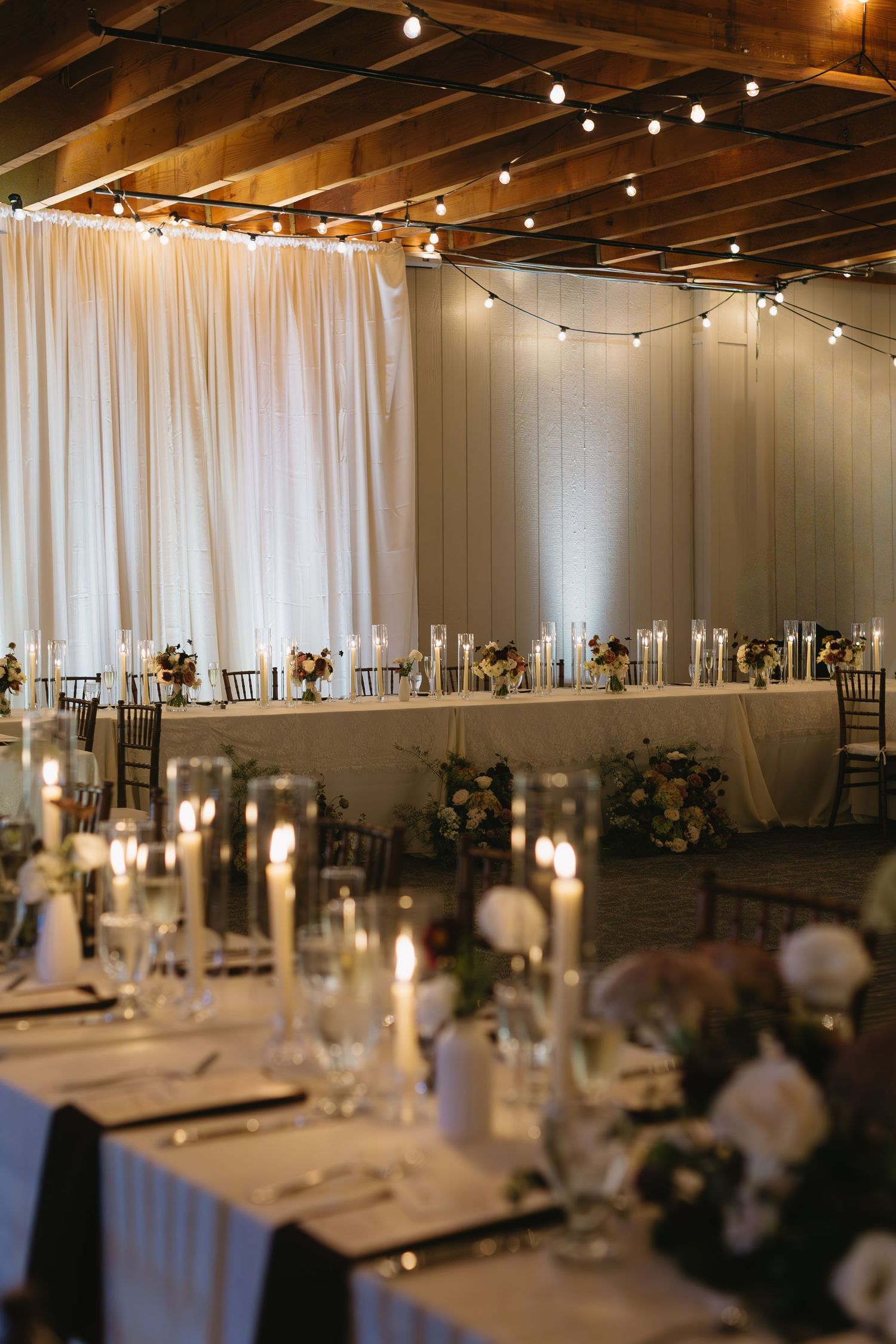 Elegant wedding reception venue with white draping, string lights, and formal table settings.