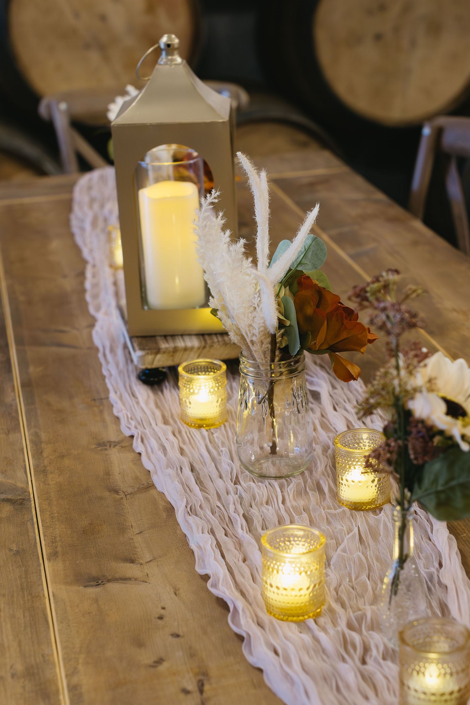 Rustic wooden table decorated with white lace runners, glowing candle lanterns, and delicate floral arrangements.